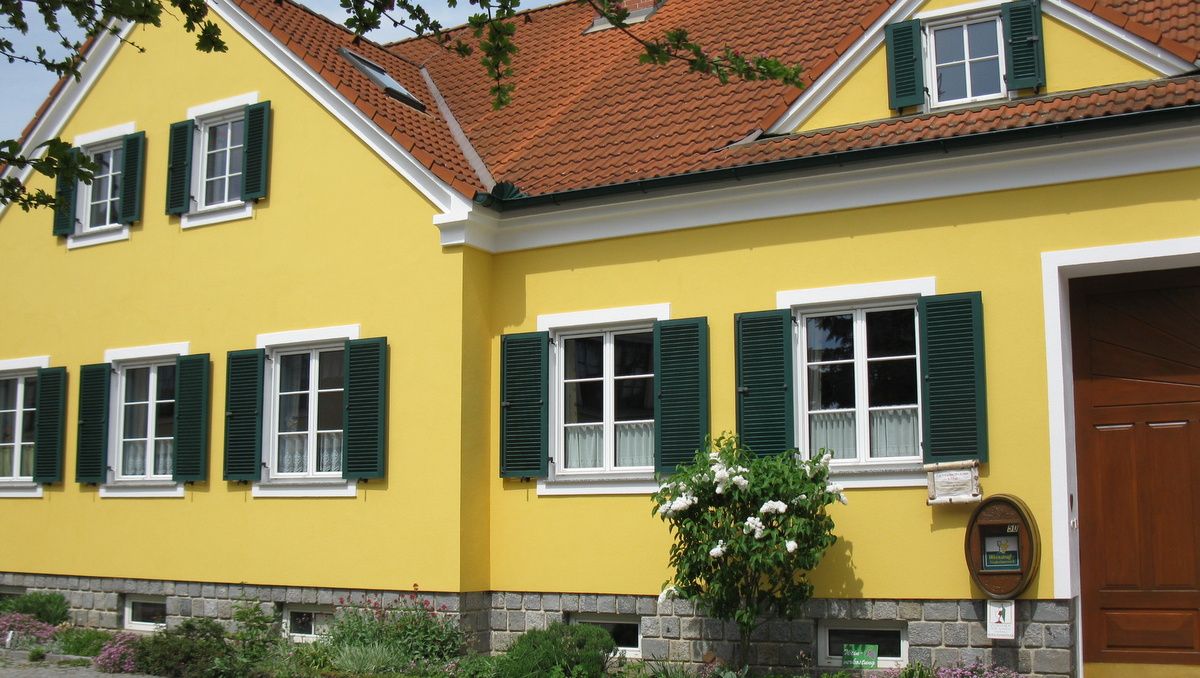 Gelbes Haus mit grünen Fensterläden und rotem Ziegeldach.