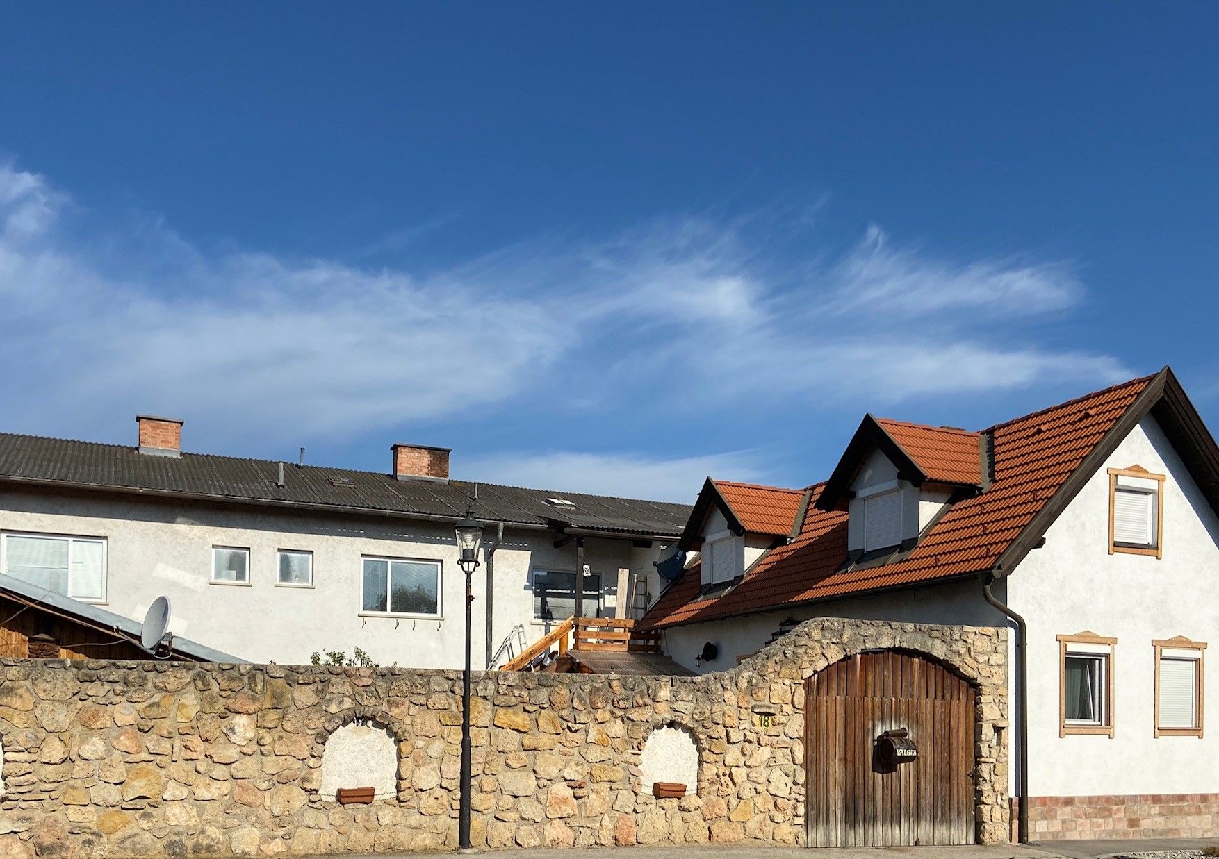 Ein Gebäude mit roten Ziegeldächern und einer Steinmauer im Vordergrund unter blauem Himmel.