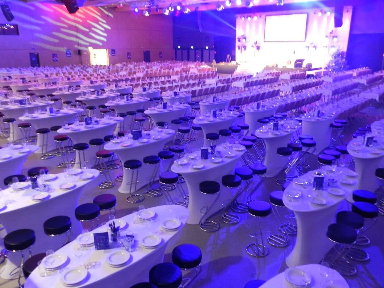 Großer Saal mit gedeckten Tischen und Stühlen, beleuchtet in Blau und Lila.