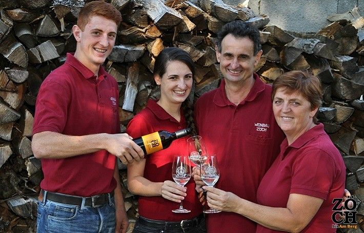 Vier Personen in roten Hemden stoßen mit Weingläsern an, vor einem Stapel Holzscheite.