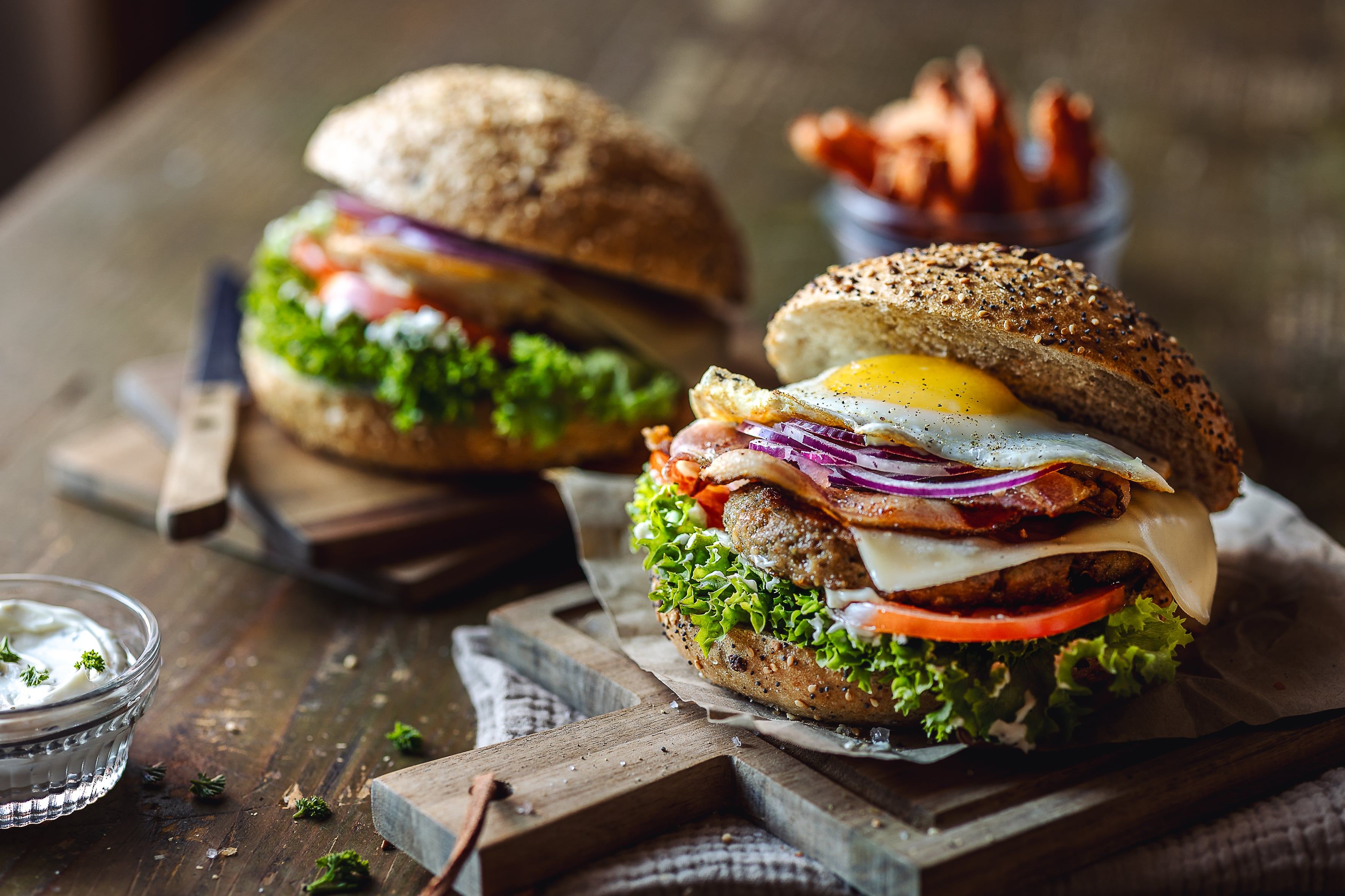 Zwei Burger mit Salat, Tomaten, Zwiebeln, Käse und Spiegelei auf einem Holztisch.