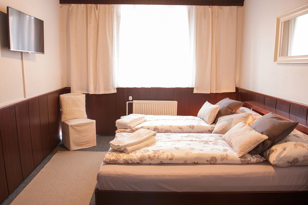 Gemütliches Hotelzimmer mit zwei Einzelbetten, Fernseher, Stuhl und Fenster mit Vorhängen.