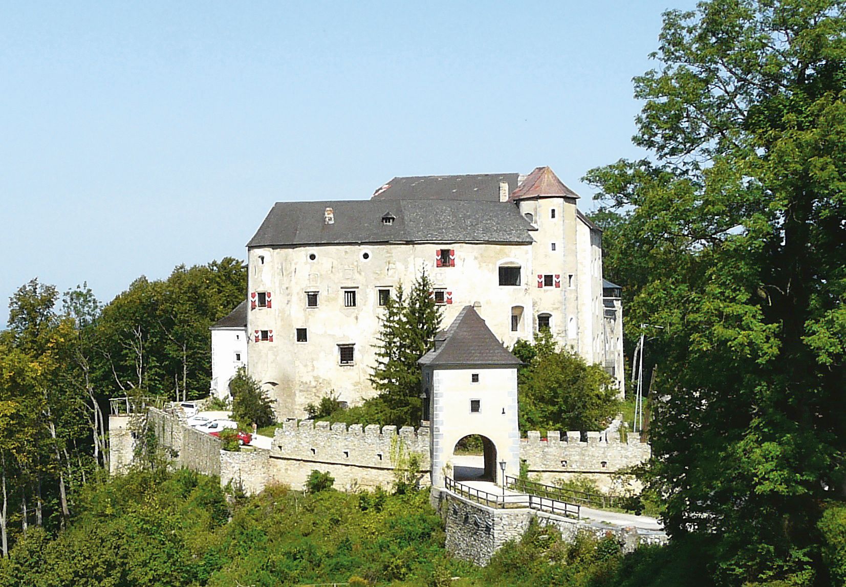 Historische Burg mit weißer Fassade und Zinnen, umgeben von Bäumen.
