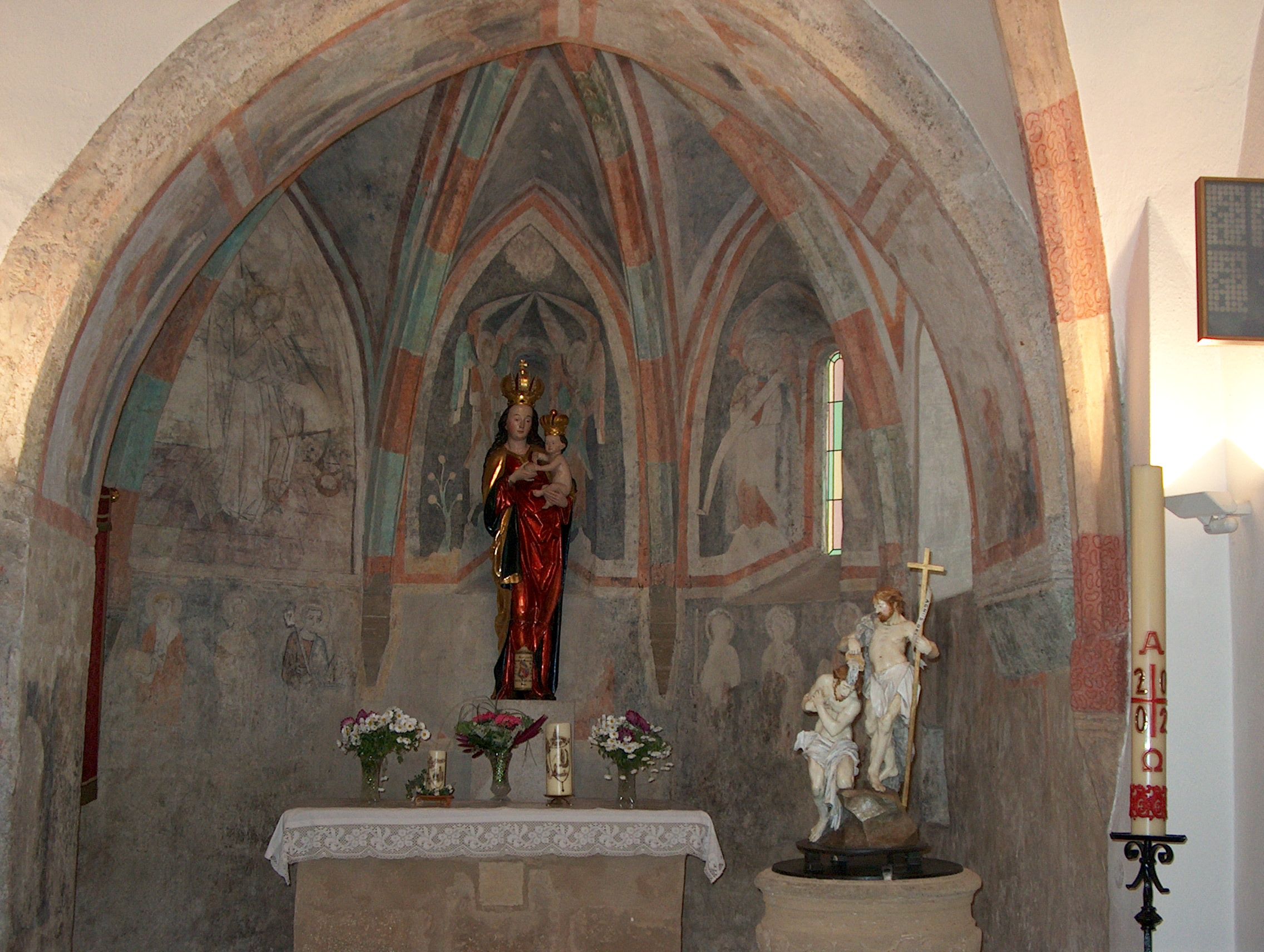 Innenansicht einer Kapelle mit Wandmalereien und religiösen Statuen.