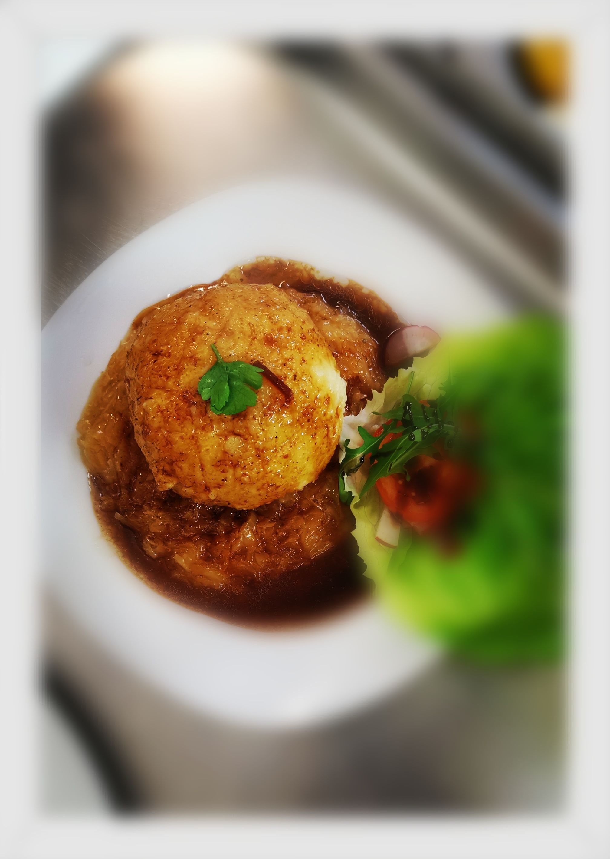 Ein Teller mit einem großen Knödel in Bratensoße, garniert mit Petersilie, und einem Salat mit Tomaten und Radieschen.