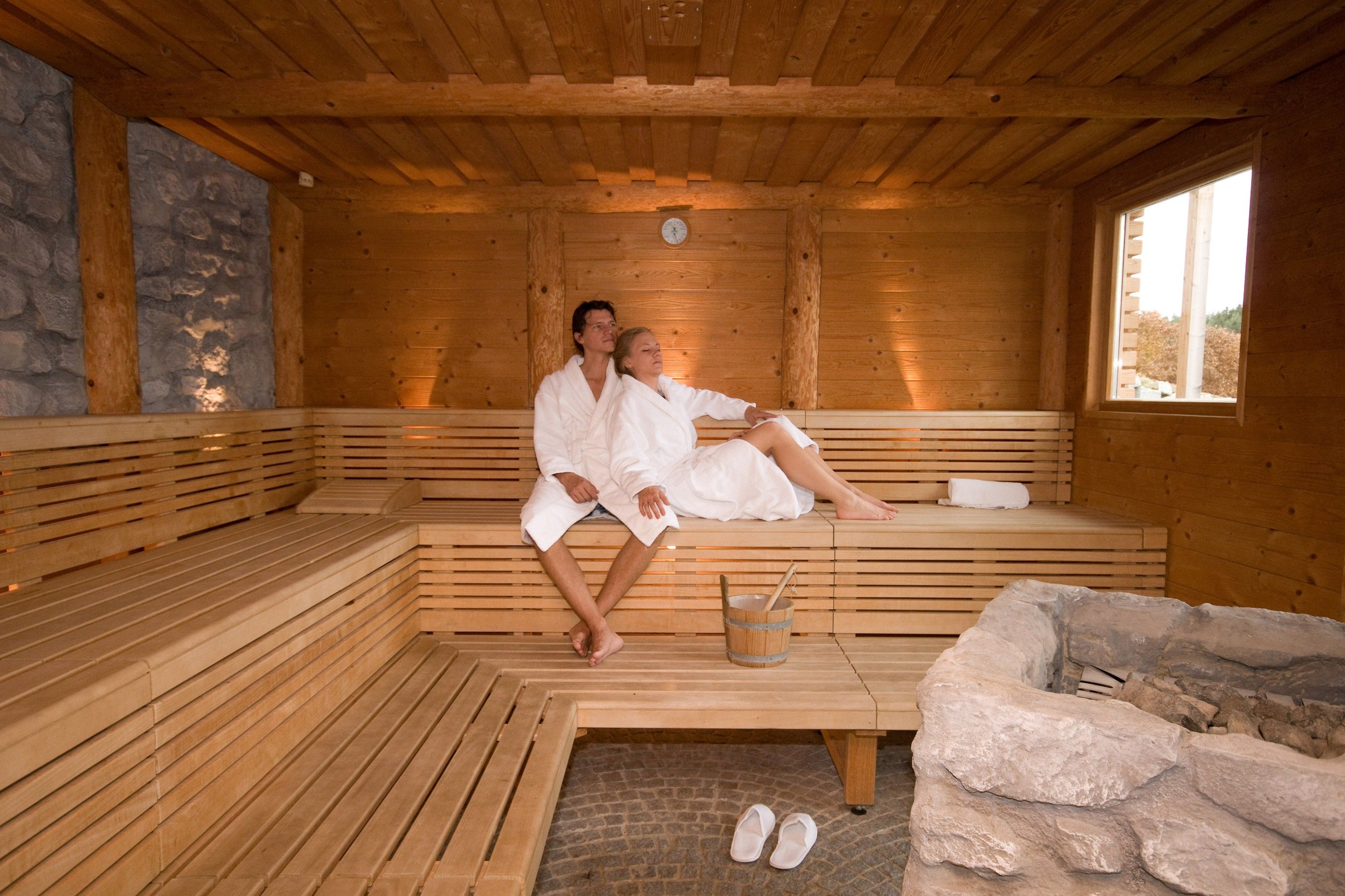 Ein Paar in weißen Bademänteln entspannt in einer Holzsauna.