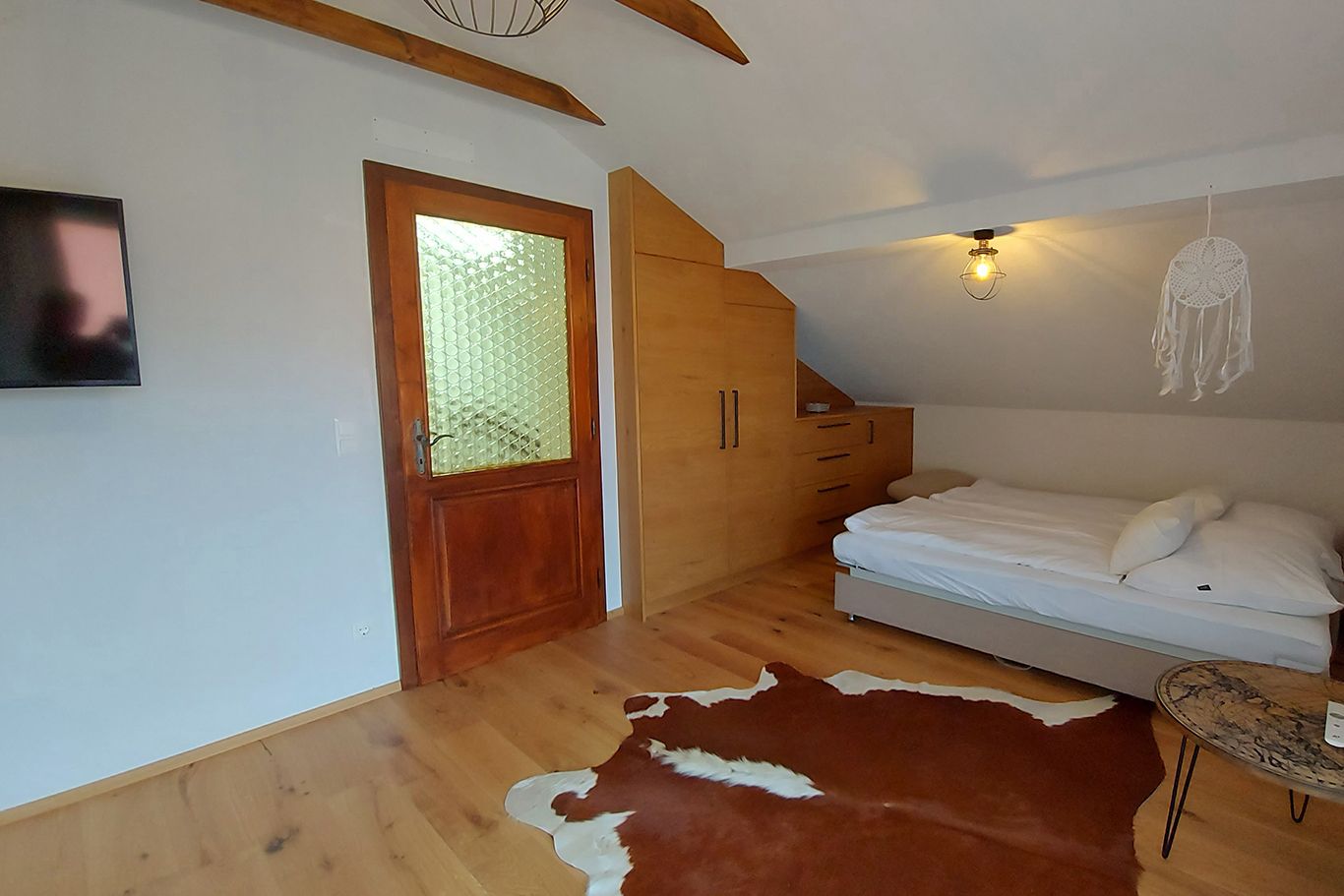 Schlafzimmer mit Holzboden, Bett, Schrank, Tür und Fernseher.