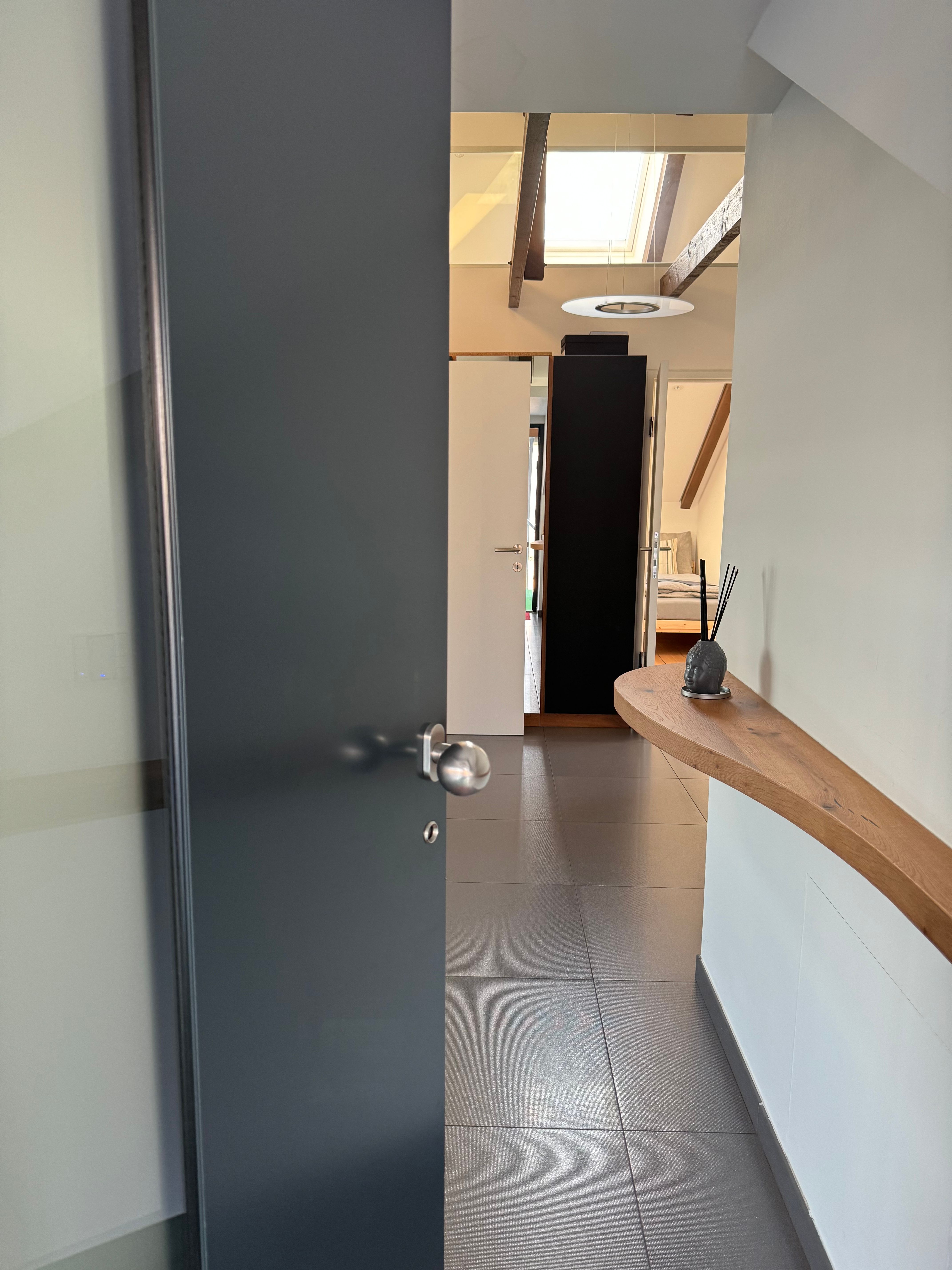 Moderner Eingangsbereich mit offener Tür, Fliesenboden und Holzregal an der Wand.