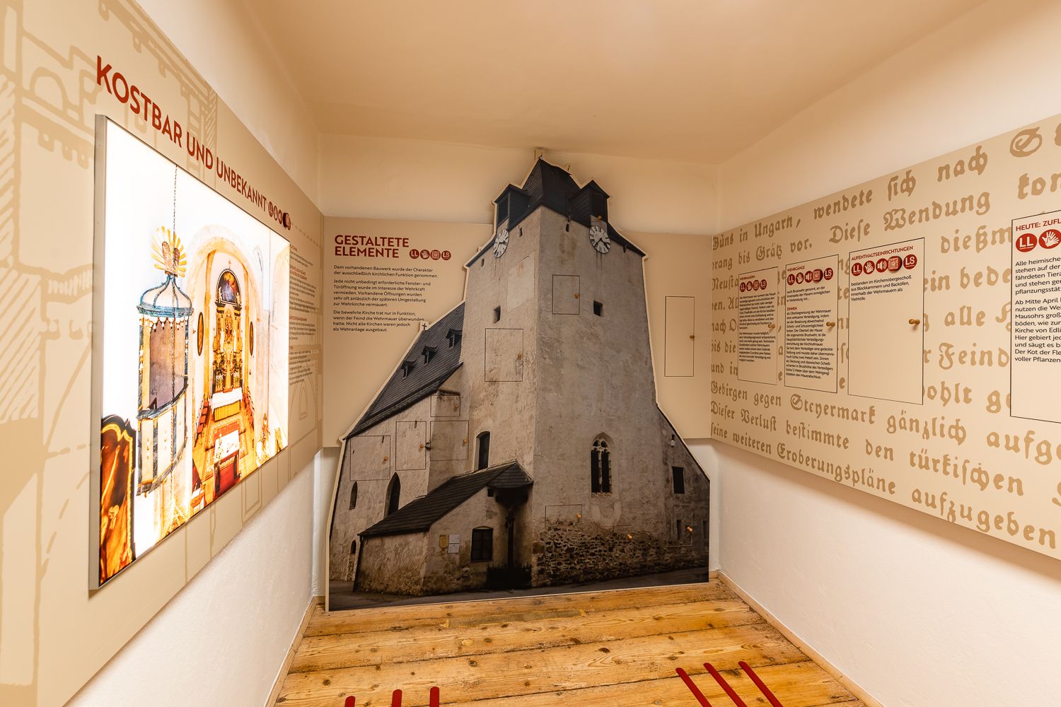 Innenansicht einer Ausstellung über Wehrkirchen mit Texttafeln und einem raumhohen Bild einer Kirche.