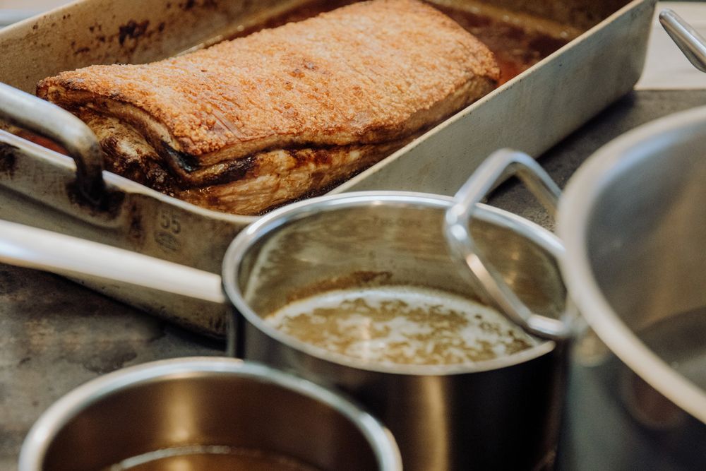Knuspriger Schweinsbraten in einer Metallpfanne, daneben Töpfe mit Soße.