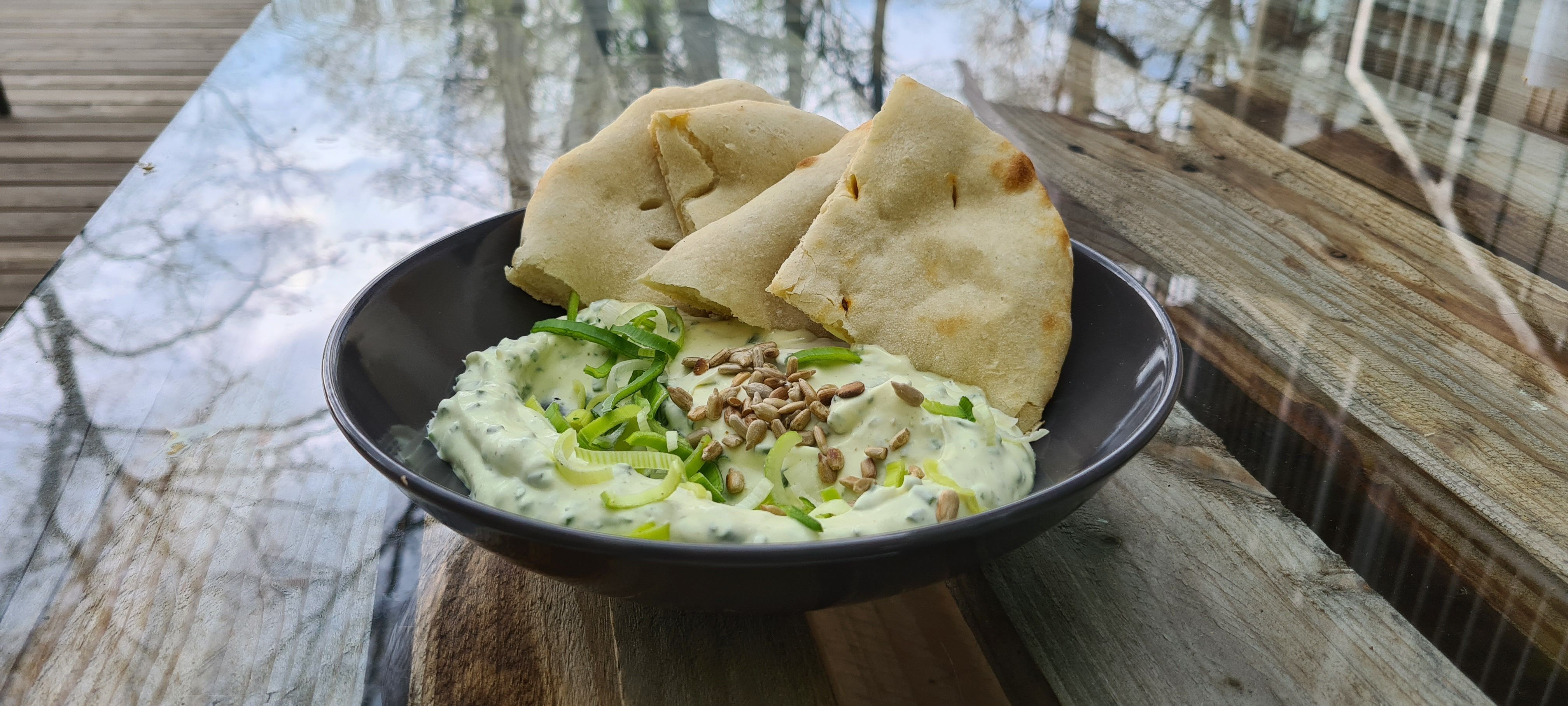 Schwarze Schale mit einem Dip und Brotecken auf einem Holztisch.