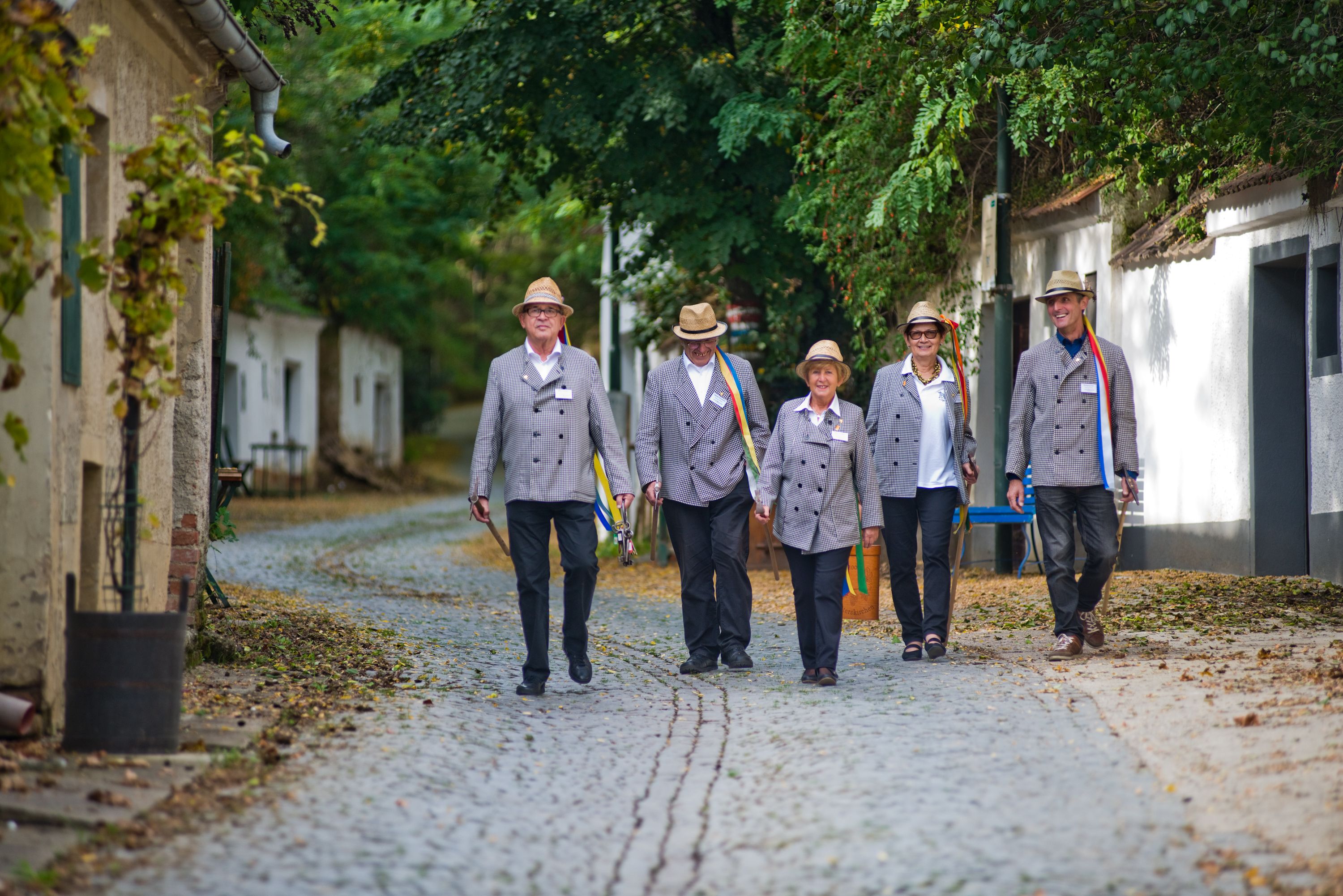 Fünf Personen in traditioneller Kleidung gehen auf einer gepflasterten Straße.
