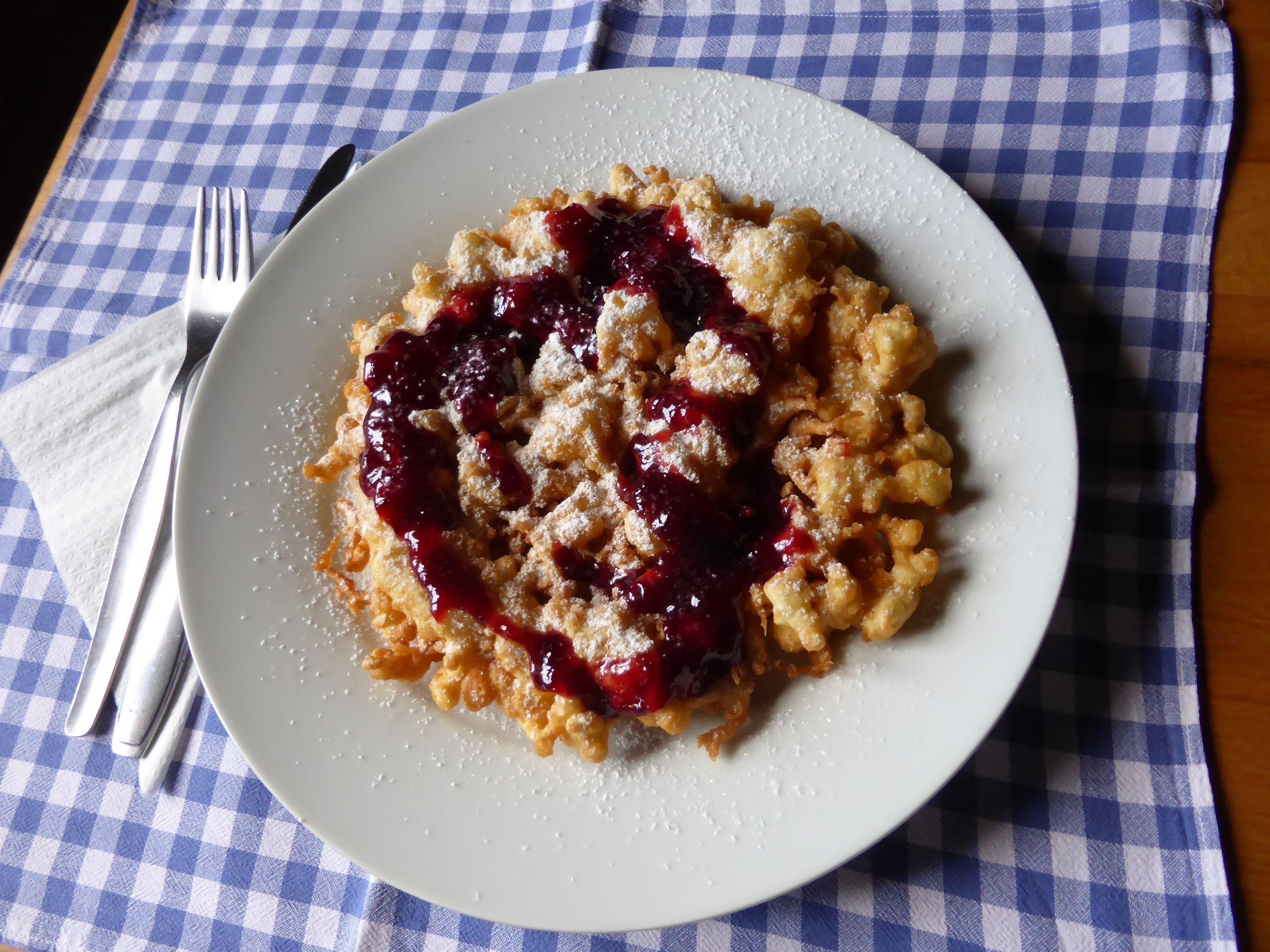 Ein Teller mit Kaiserschmarrn und roter Grütze auf einem blau-weiß karierten Tuch.