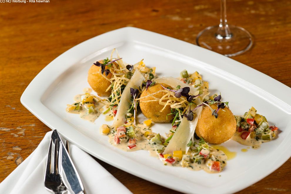 Drei goldbraune Kroketten auf einem weißen Teller, garniert mit Gemüse und Sauce.