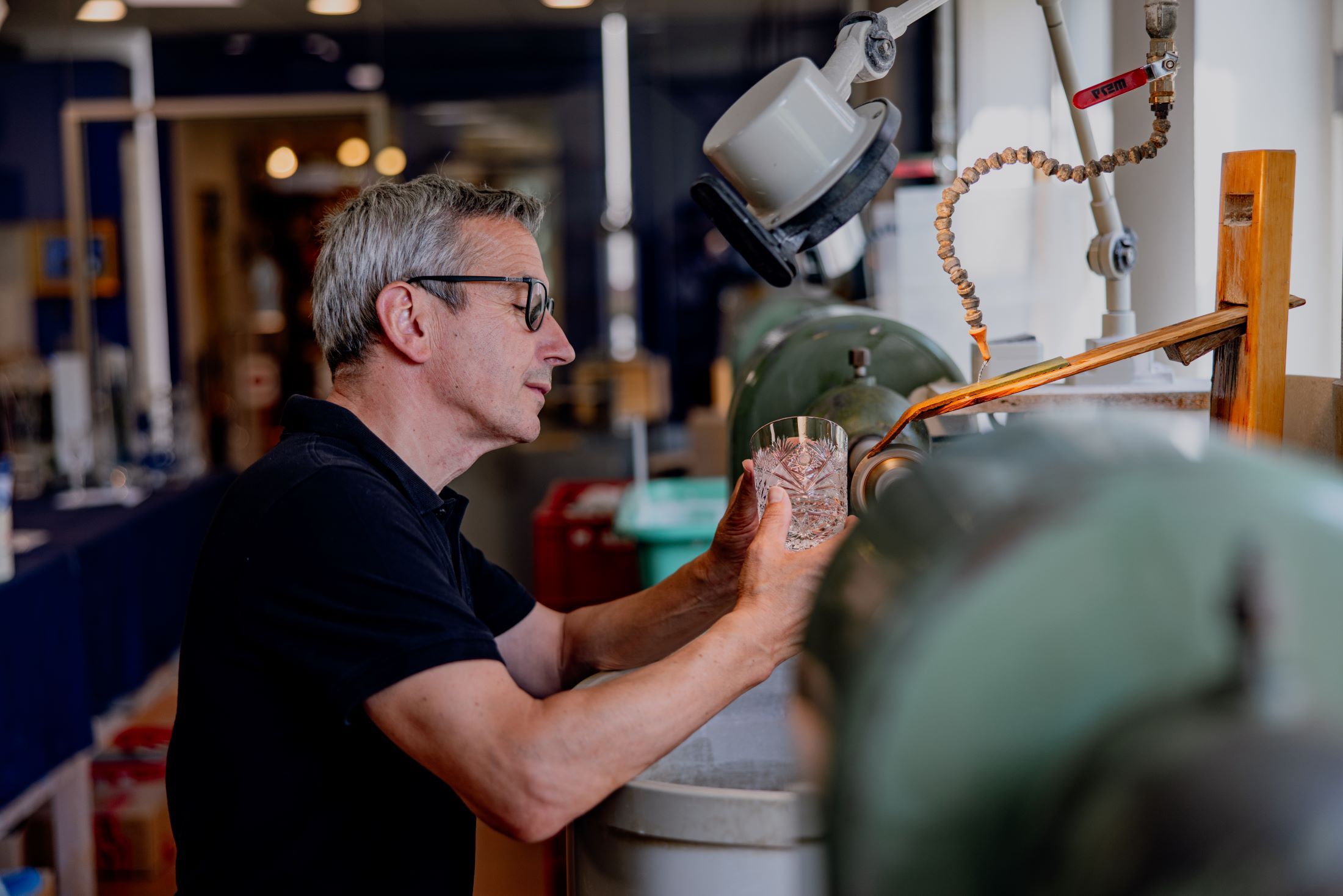 Ein Mann bearbeitet ein Glas an einer Schleifmaschine in einer Werkstatt.