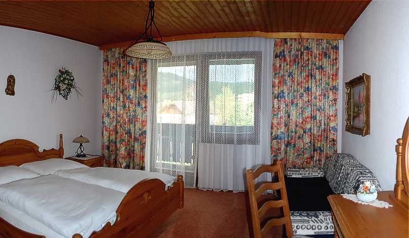 Gemütliches Hotelzimmer mit Holzmöbeln, Doppelbett, Balkon und bunten Vorhängen.