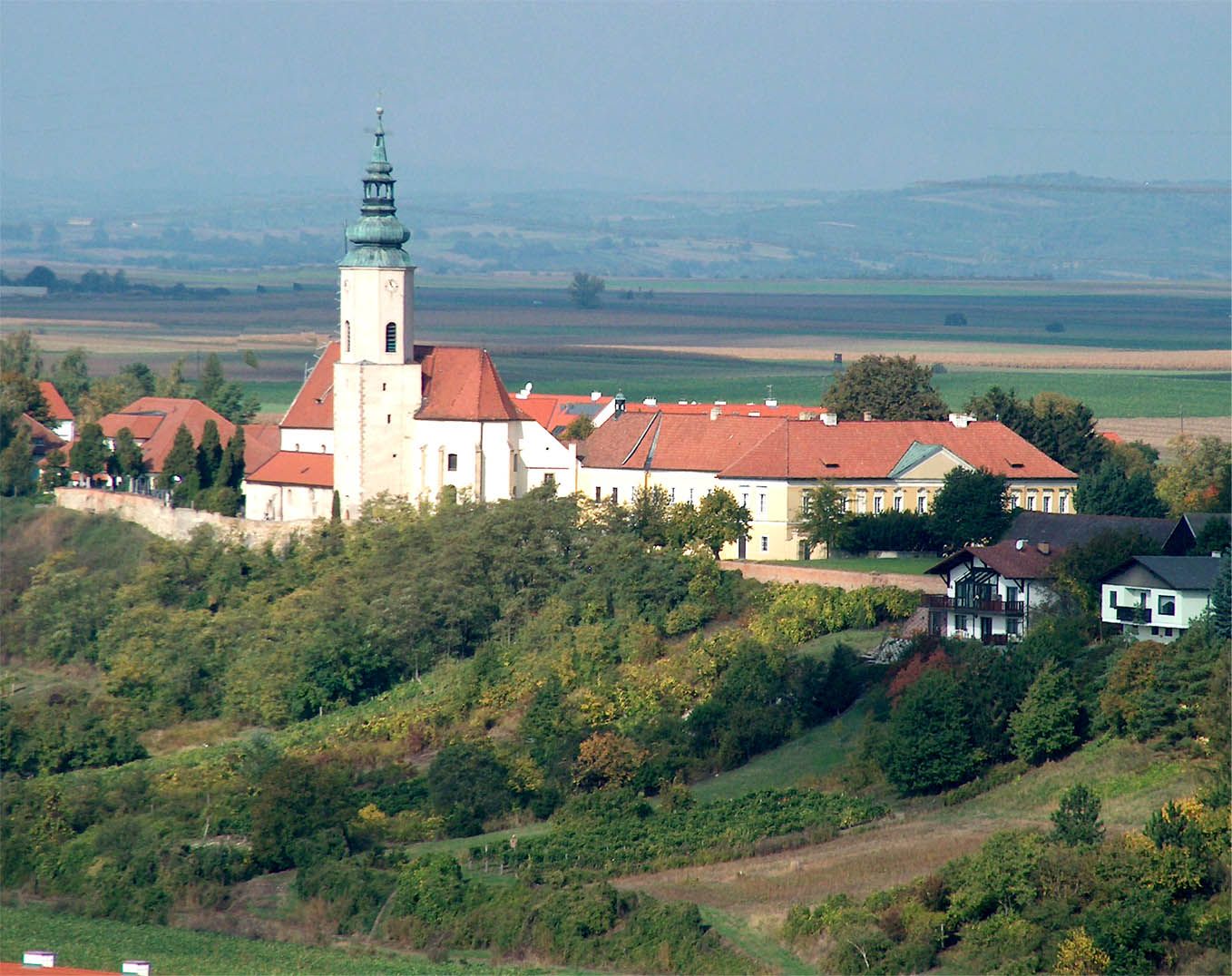 Pfarrkirche St. Agatha auf einem Hügel mit umliegenden Gebäuden und Landschaft im Hintergrund.