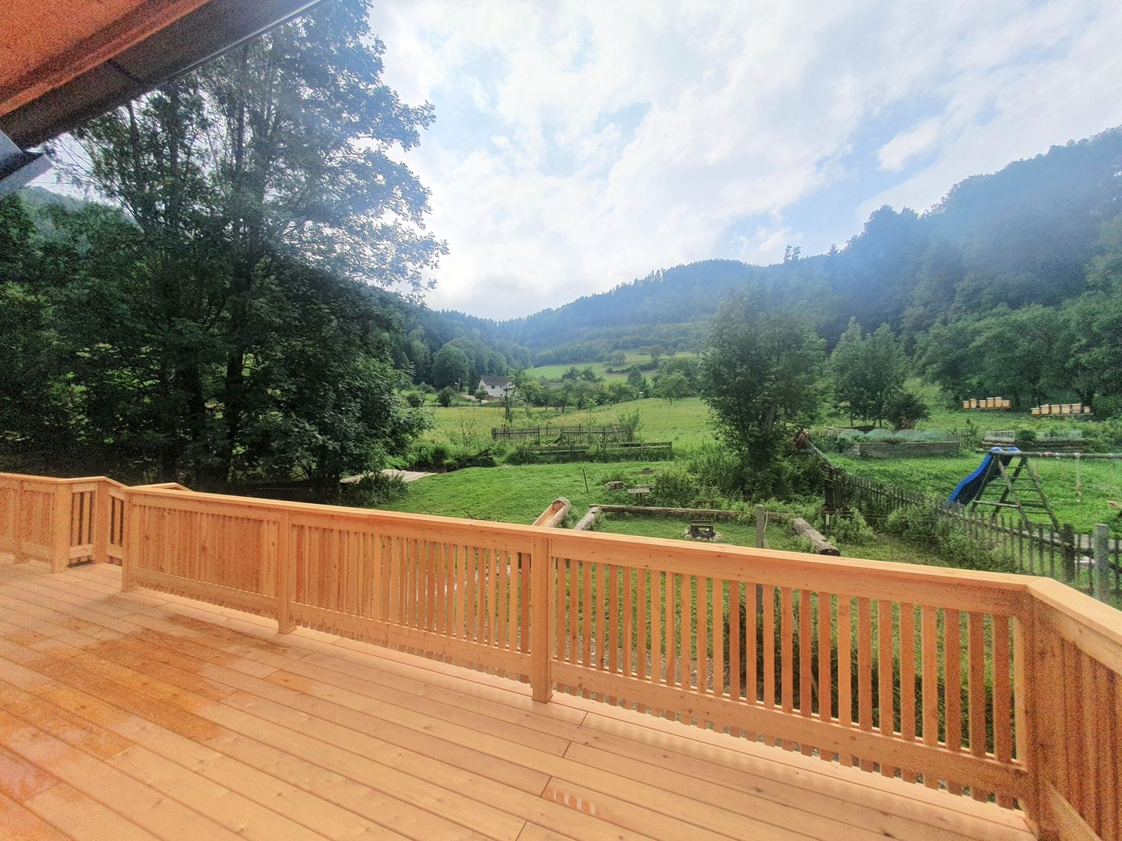 Blick von einer Terrasse auf eine grüne Landschaft mit Bäumen und Hügeln.