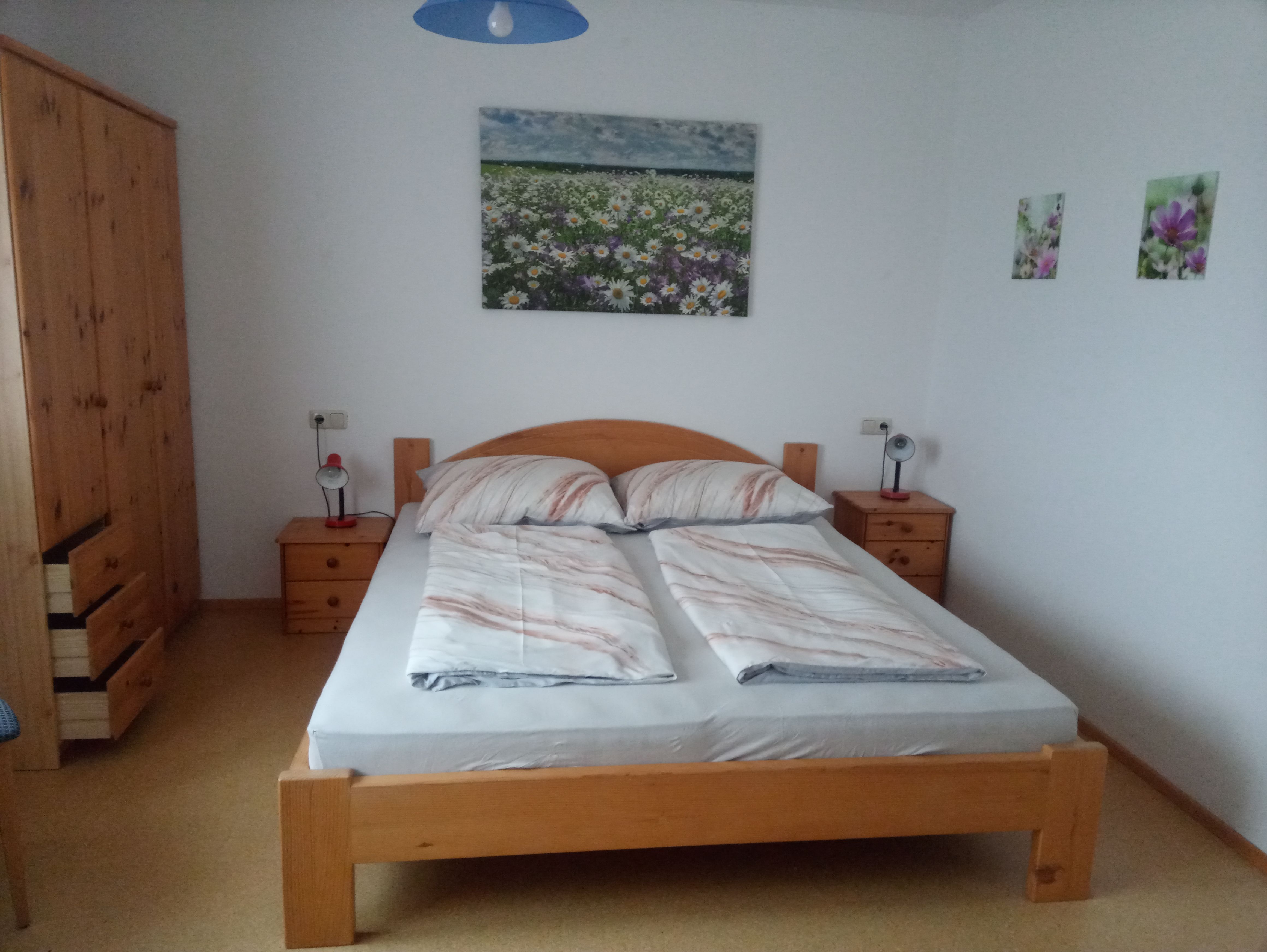 Schlafzimmer mit Doppelbett, Holzmöbeln und Blumenbildern an der Wand.