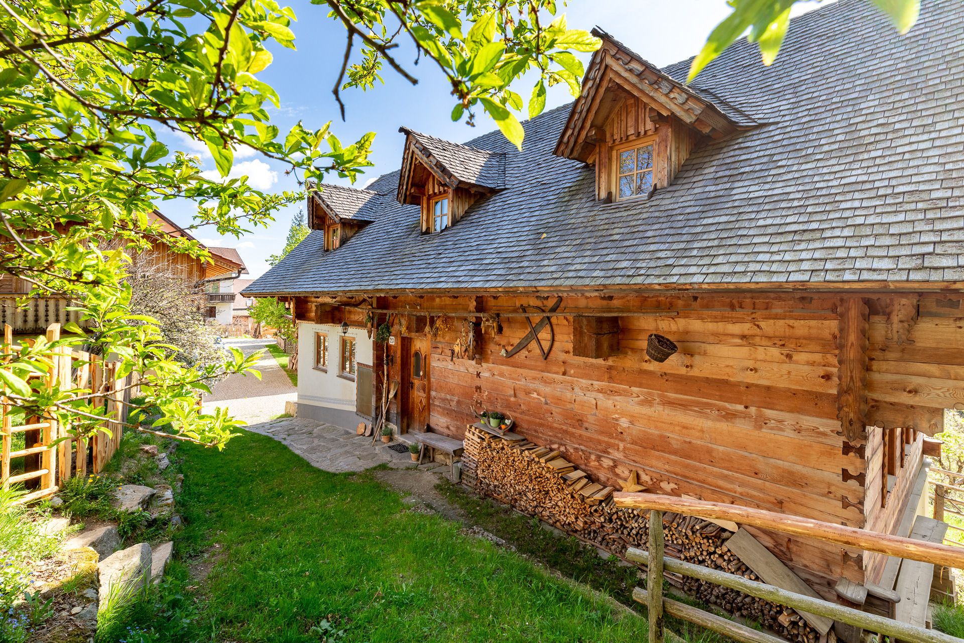 Traditionelles Holzhaus mit Holzstapel und Holzzaun umgeben von grüner Natur.