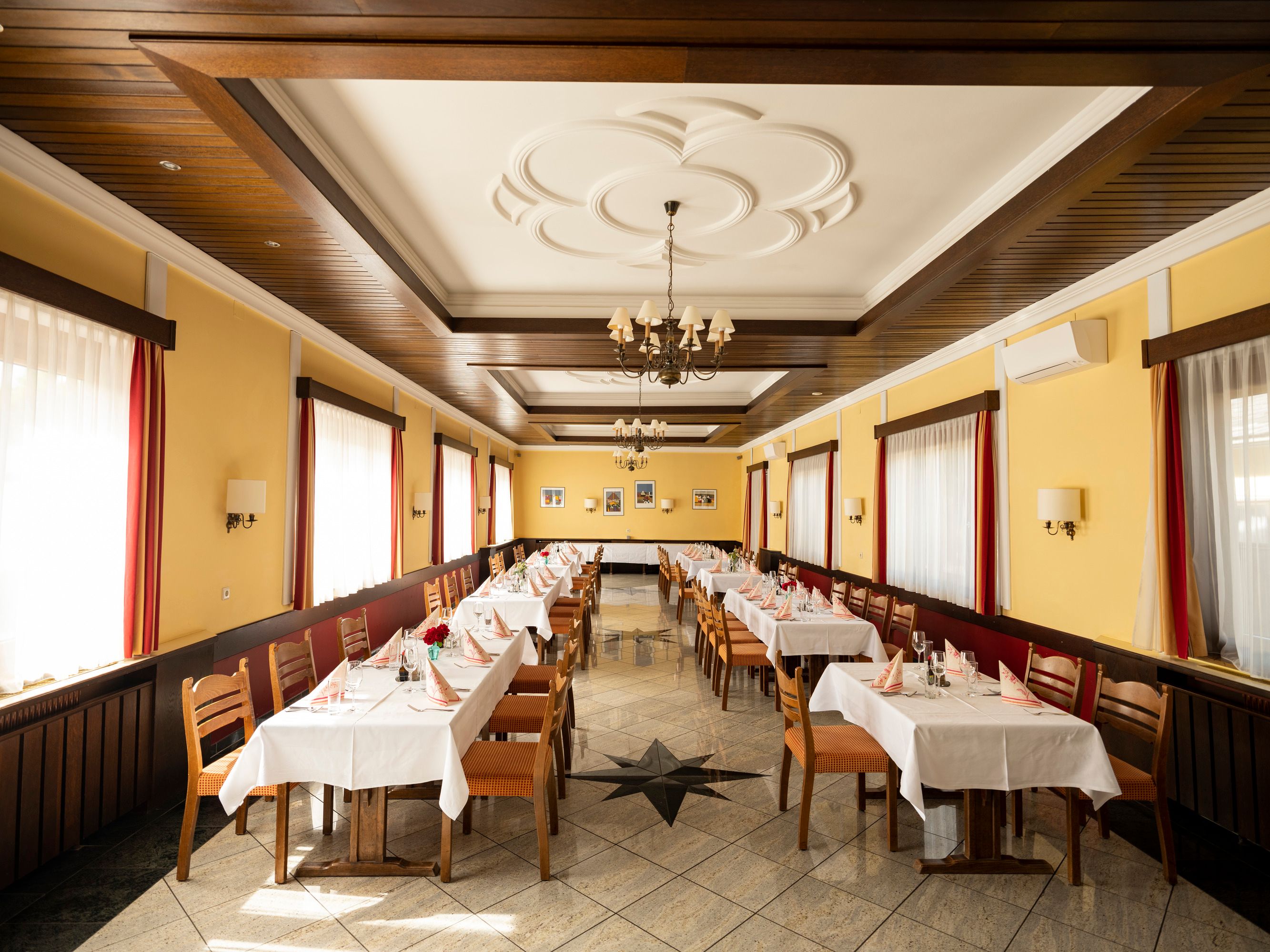 Ein festlich gedeckter Speisesaal mit gelben Wänden, Holzmöbeln und weißen Tischdecken.