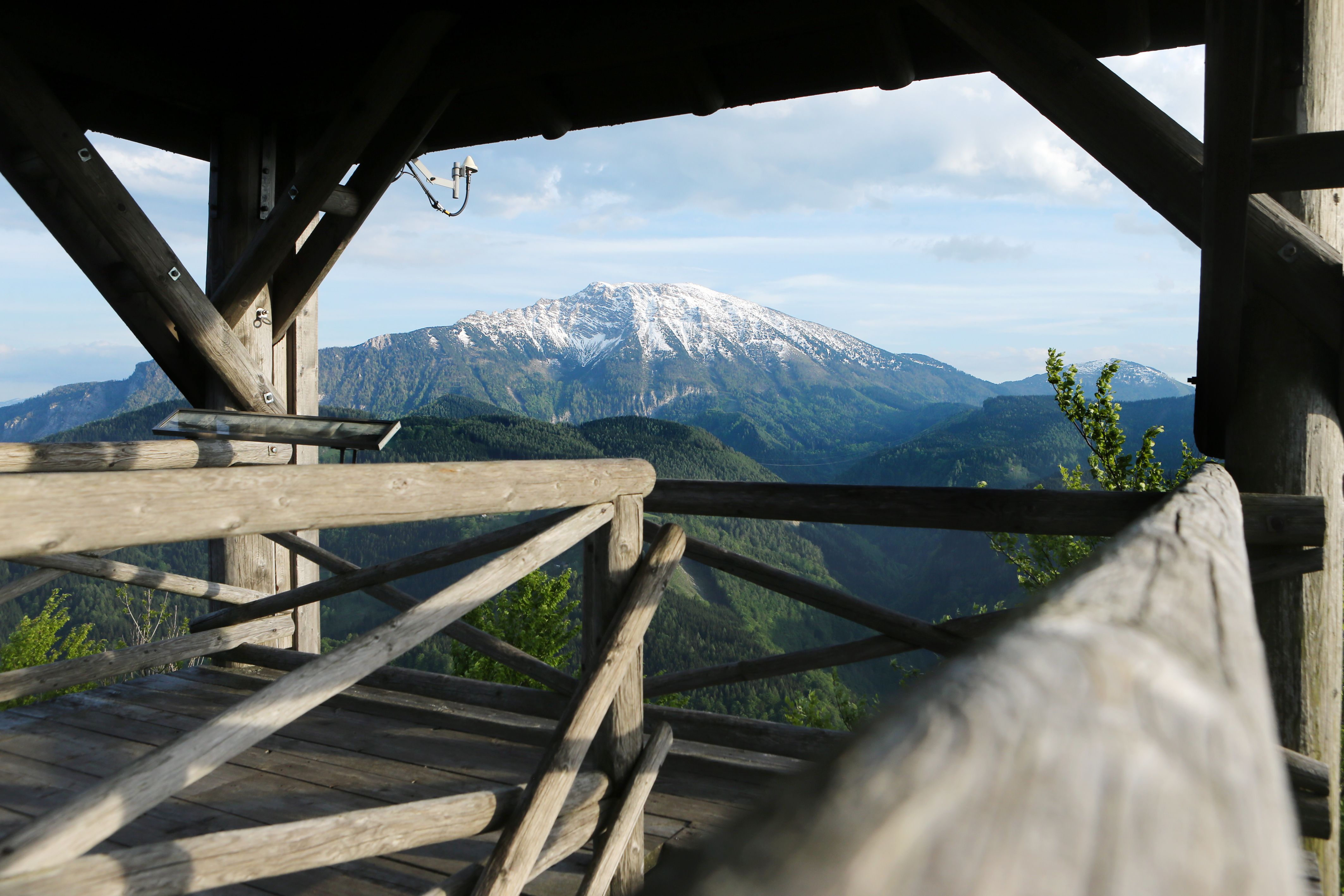 Holzplattform mit Blick auf schneebedeckten Berg und bewaldete Hügel.