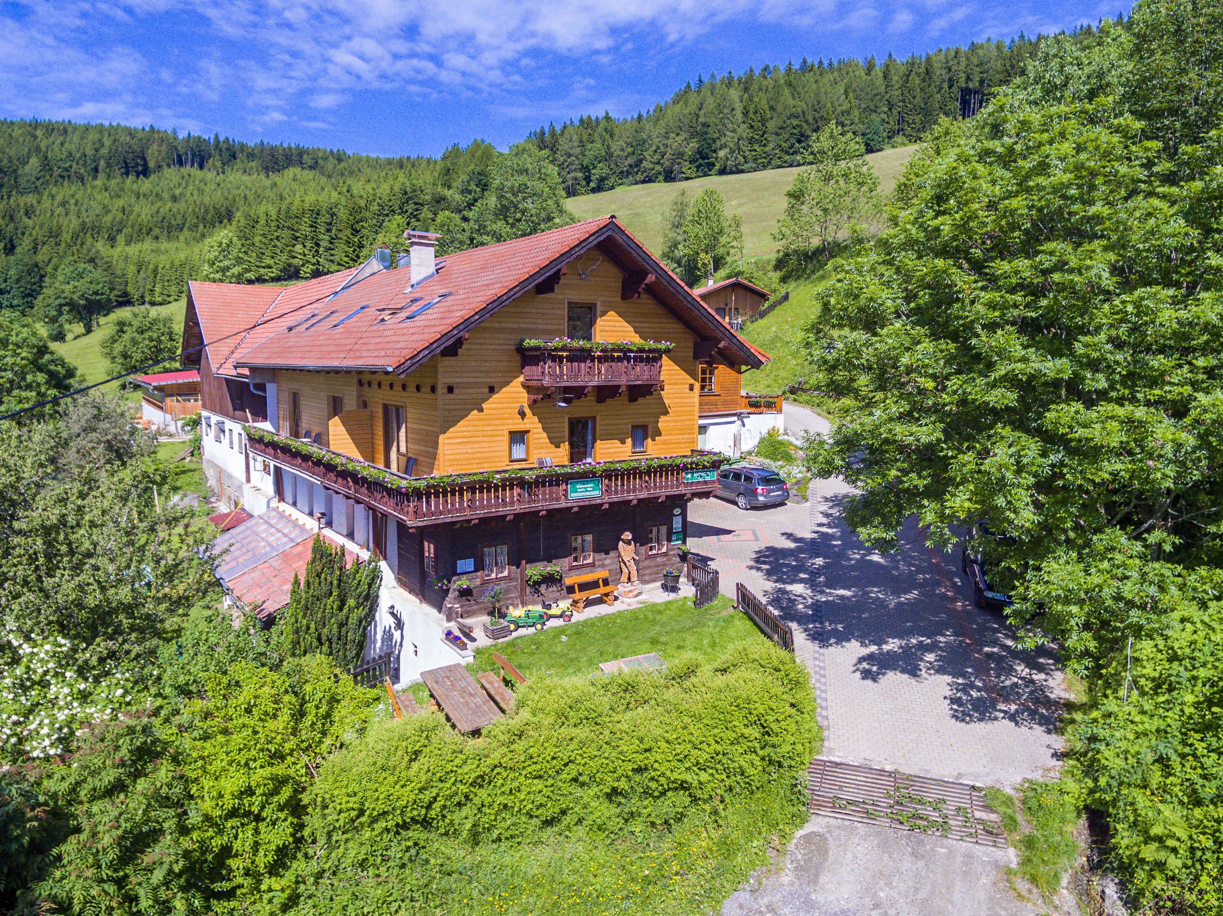 Ein traditionelles Holzhaus in einer grünen, hügeligen Landschaft mit Bäumen und einem blauen Himmel.