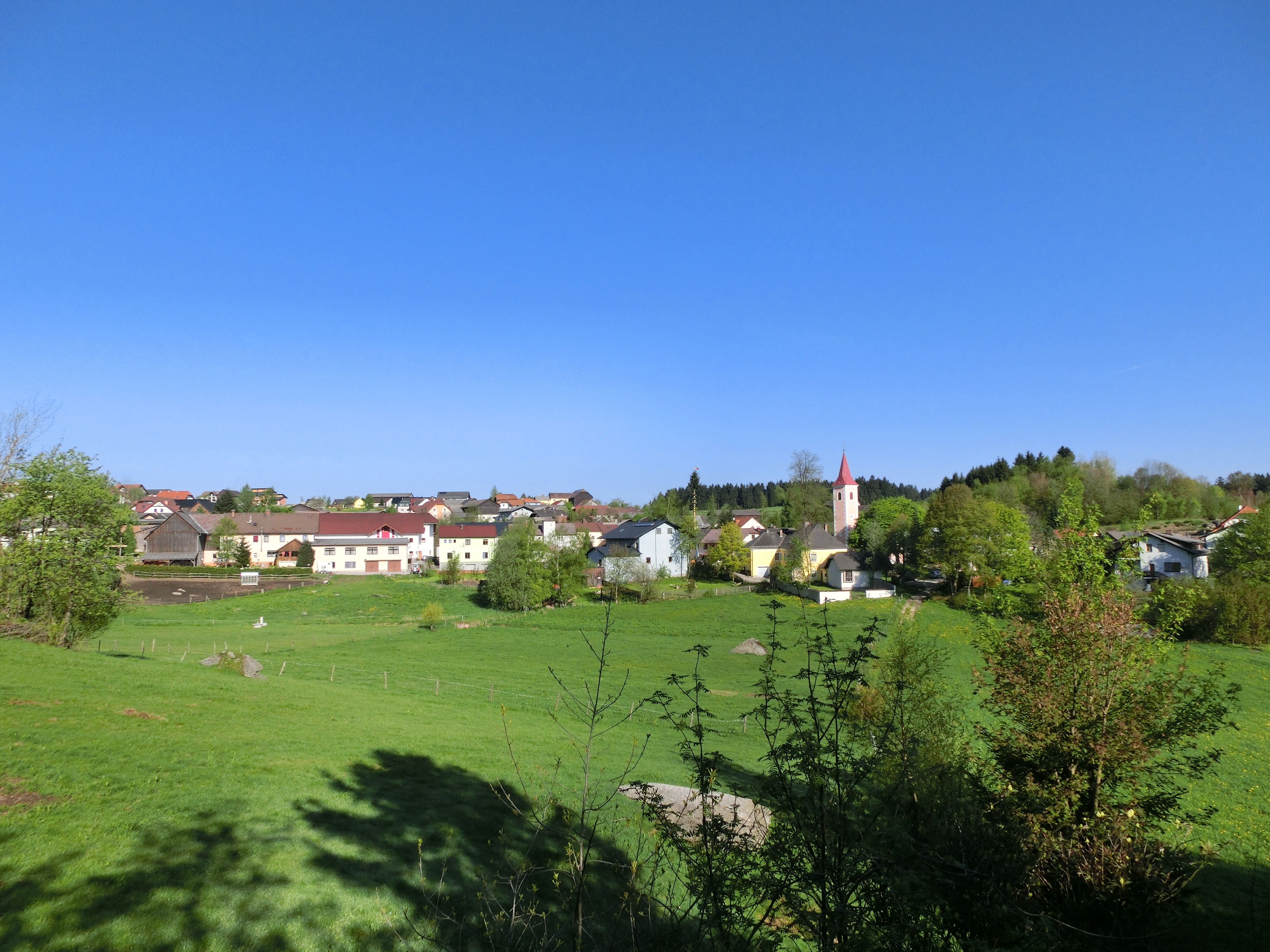 Landschaftsansicht der Marktgemeinde Altmelon mit grünen Wiesen und einer Kirche im Hintergrund.