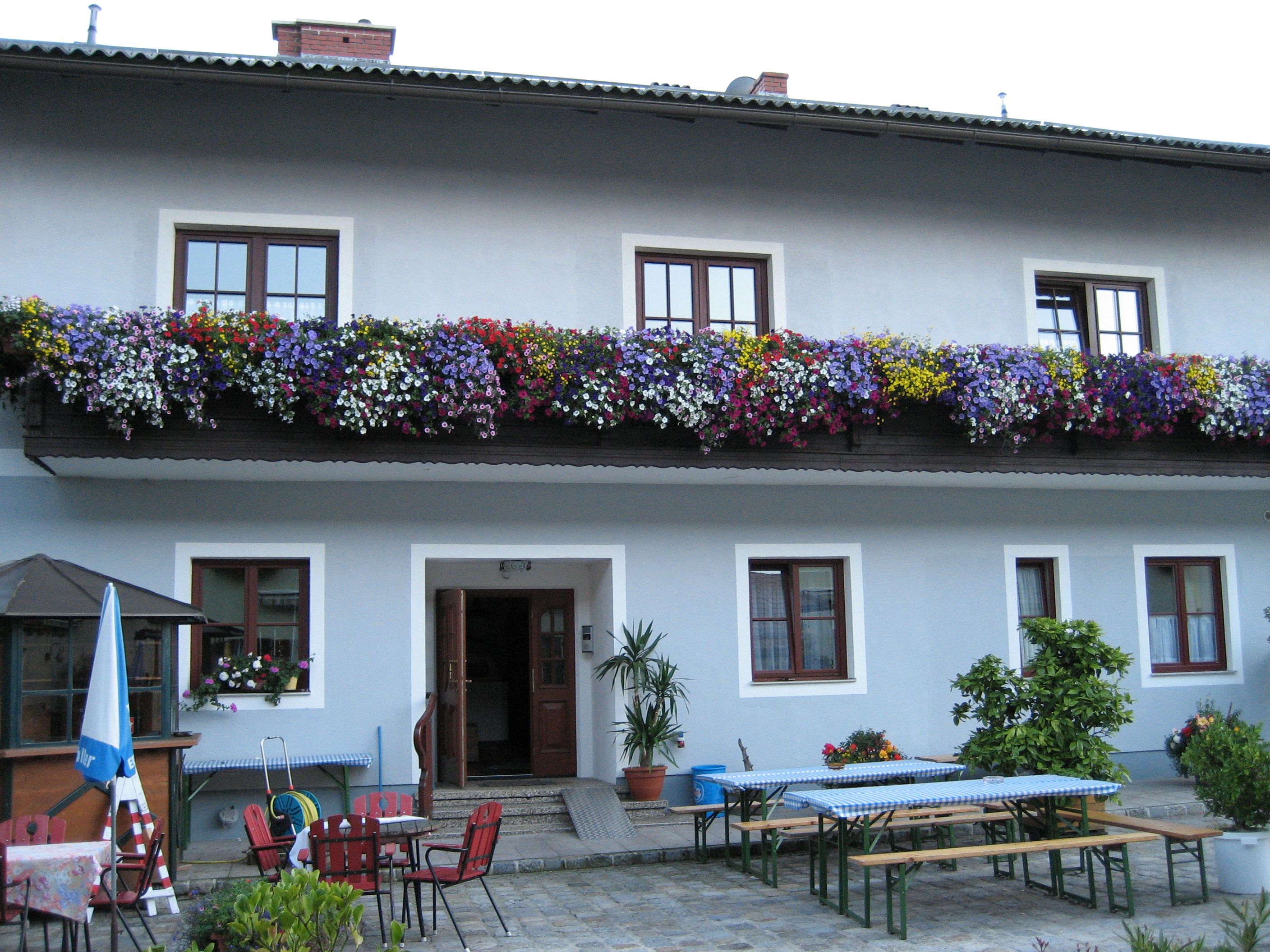 Gasthof mit blauer Fassade, Blumenkästen am Balkon und Biergartenmöbeln im Vordergrund.