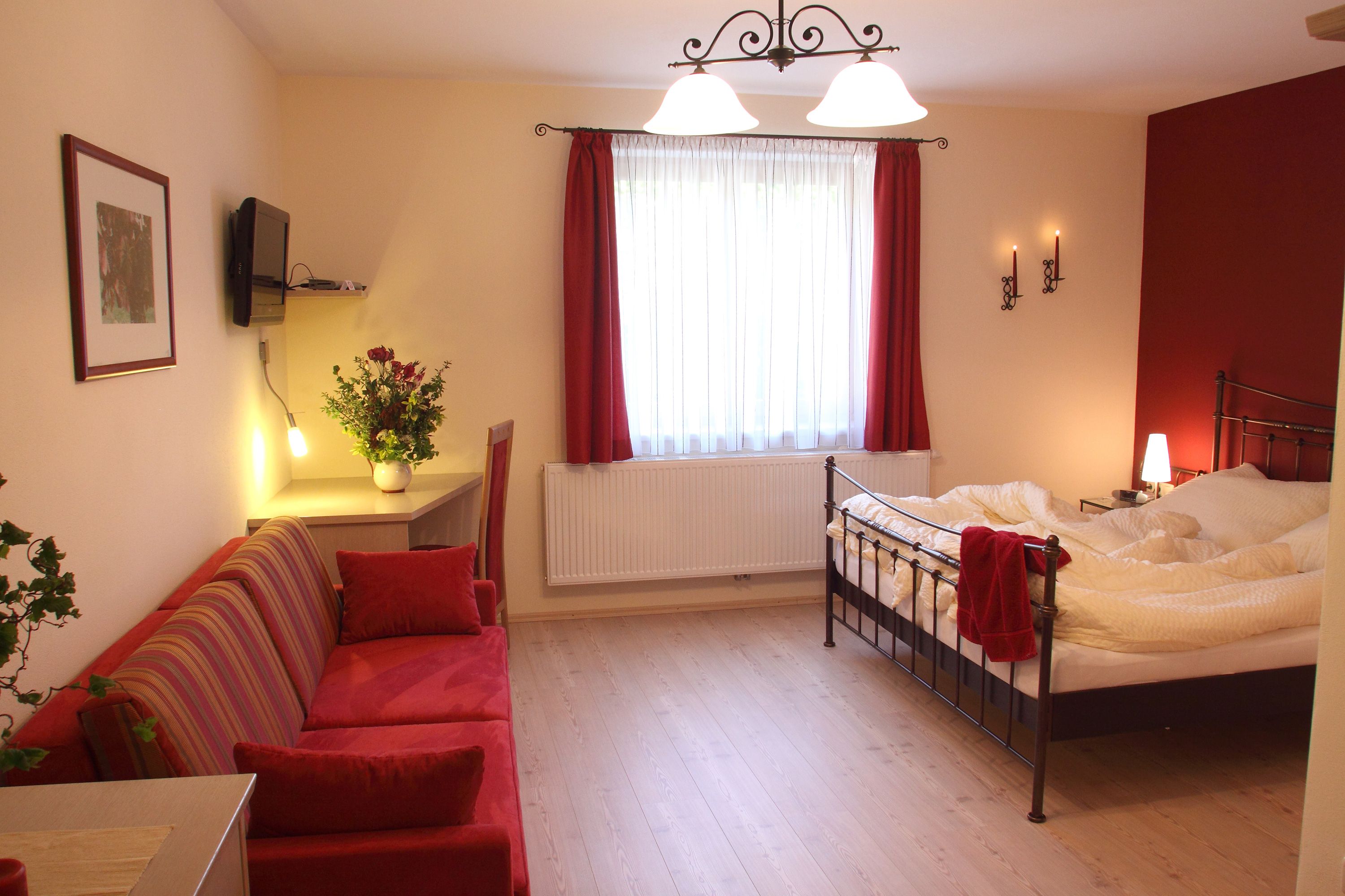 Gemütliches Hotelzimmer mit Doppelbett, rotem Sofa und Schreibtisch.