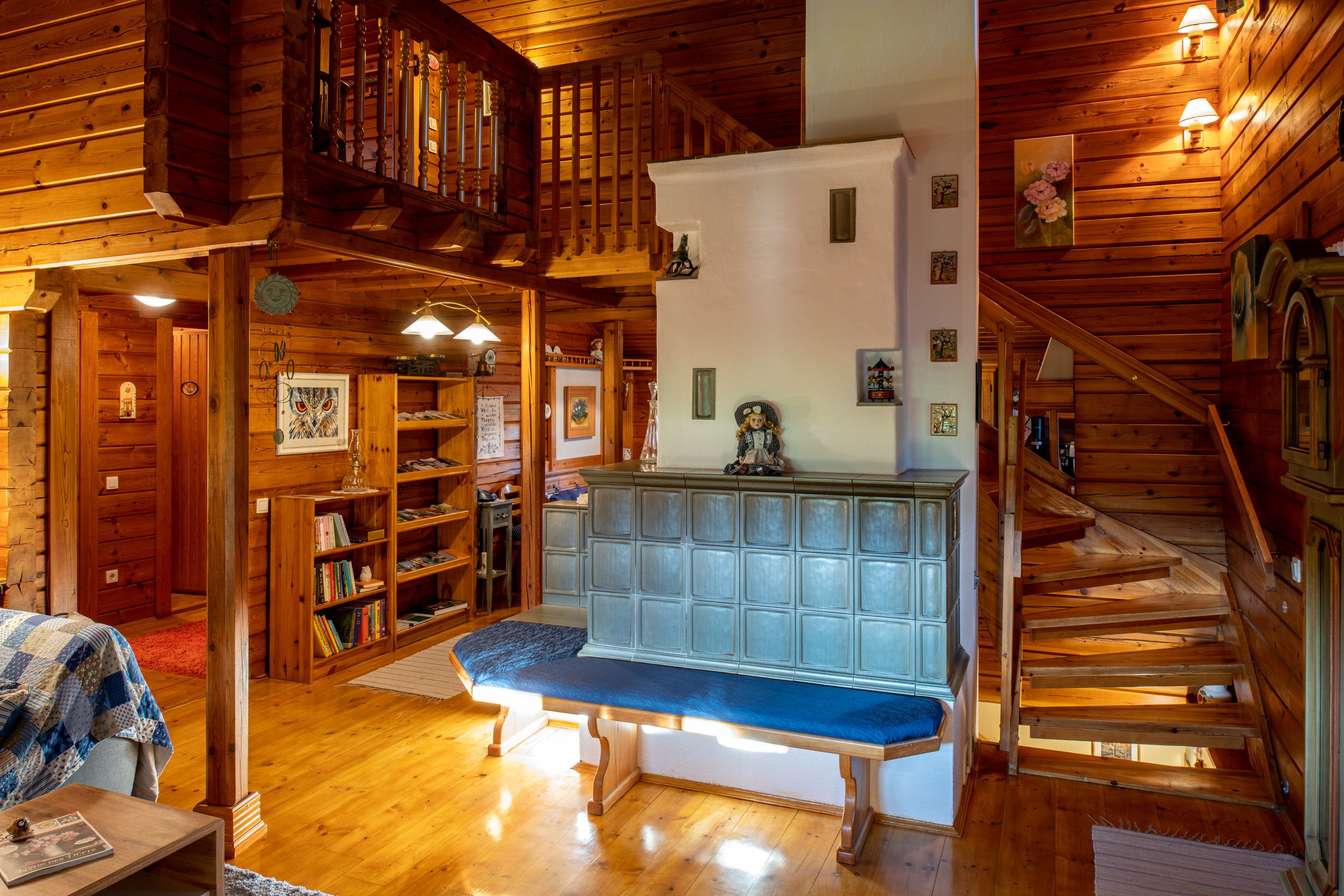 Gemütliches Wohnzimmer mit Kachelofen, Holzwänden und Treppe.