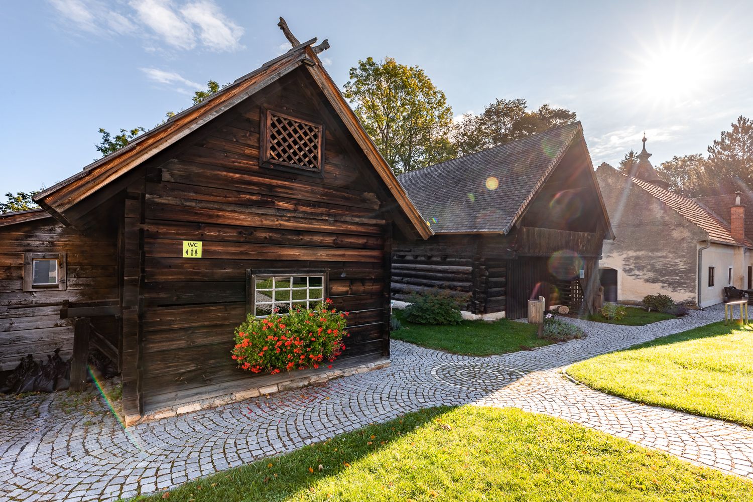Museumsdorf Krumbach mit historischen Holzhäusern, gepflastertem Weg und sonnigem Himmel.