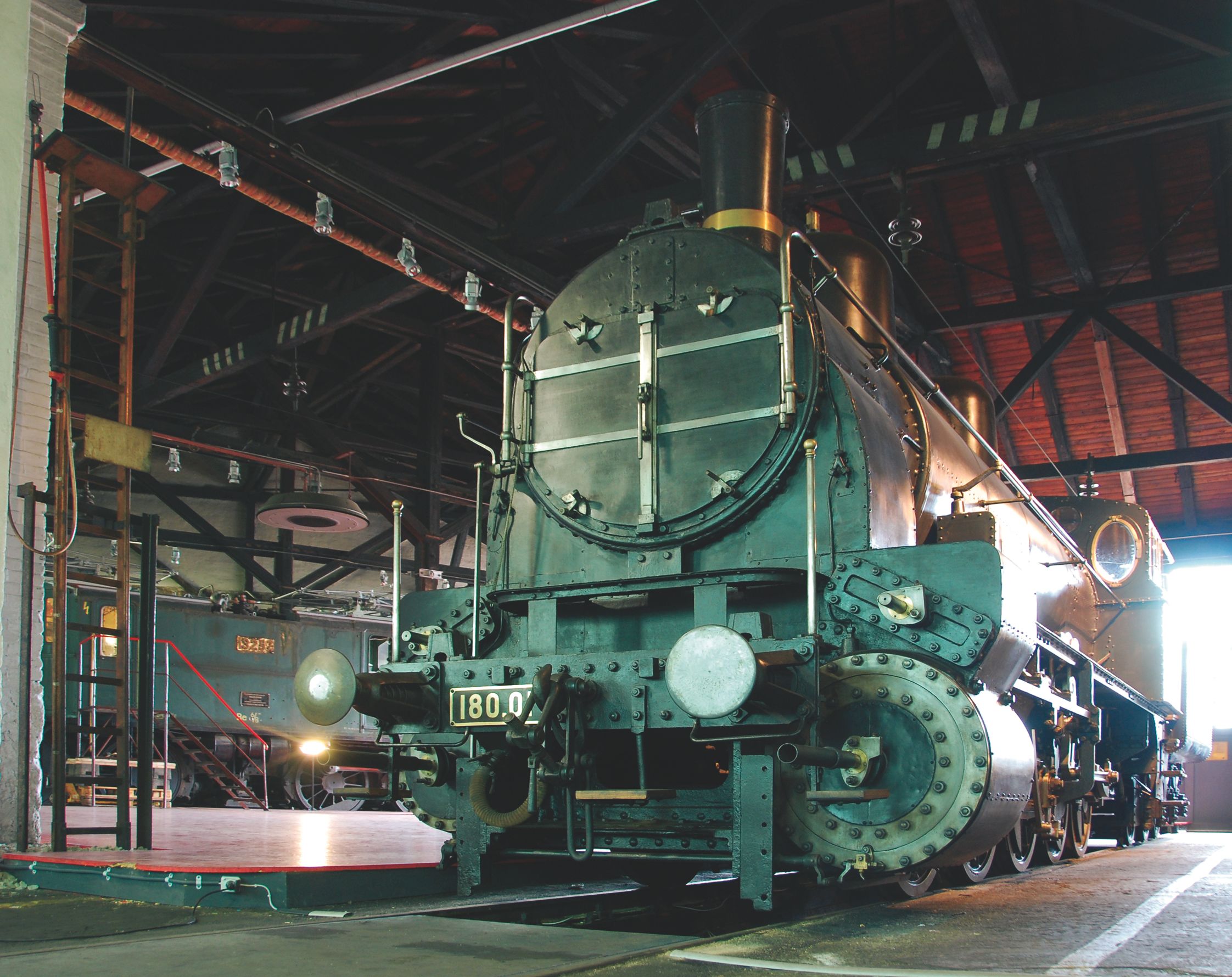 Historische Dampflokomotive 180.01 im Rundlokschuppen des Südbahn Museums, von vorn in einer Ausstellungshalle.