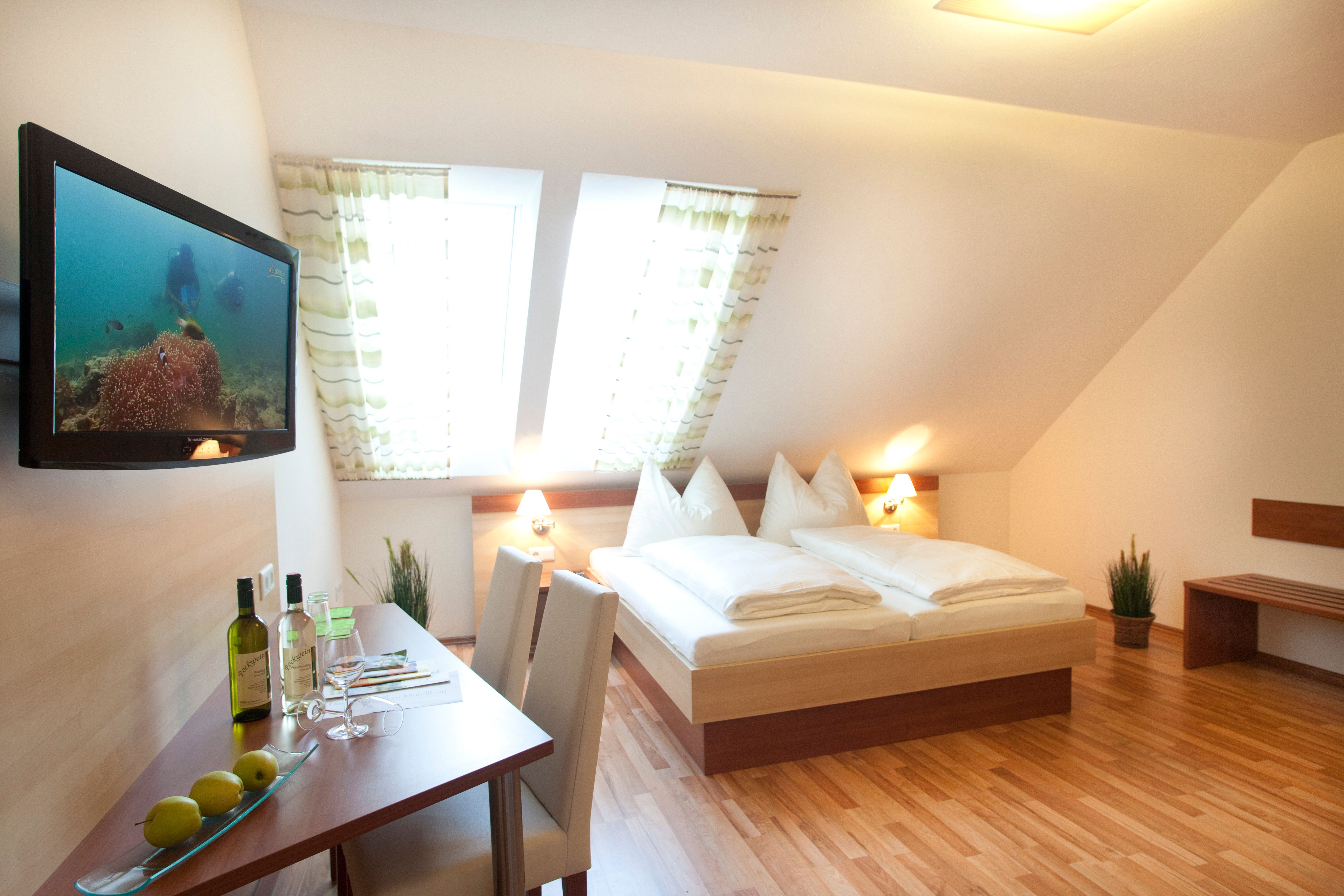 Ein gemütliches Gästezimmer mit Doppelbett, Flachbildfernseher, Tisch mit Stühlen und Dachfenstern.