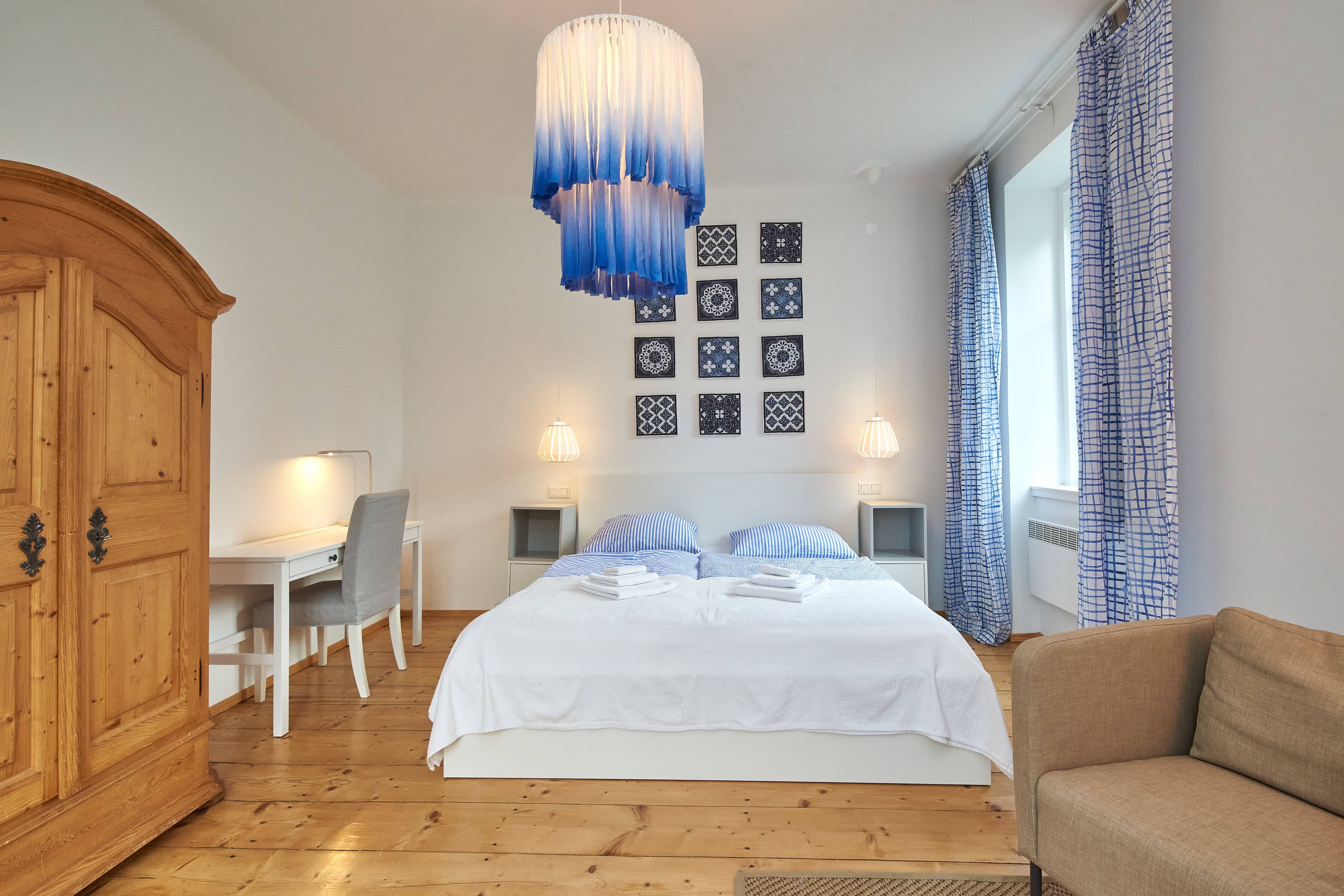 Schlafzimmer mit Doppelbett, blau-weißen Vorhängen, Holzboden und einem großen Holzschrank.