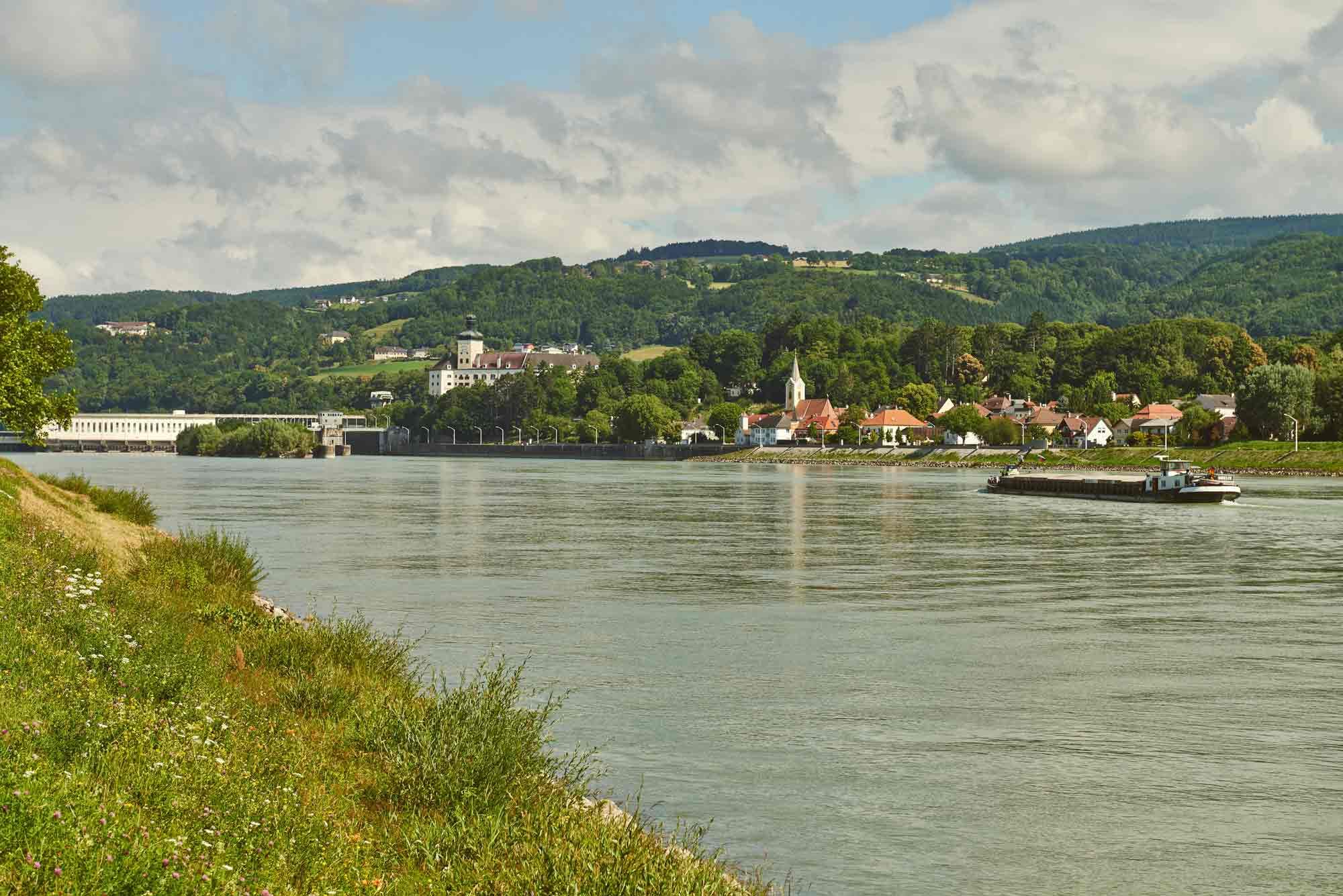 Flusslandschaft mit Dorf und Hügeln im Hintergrund.