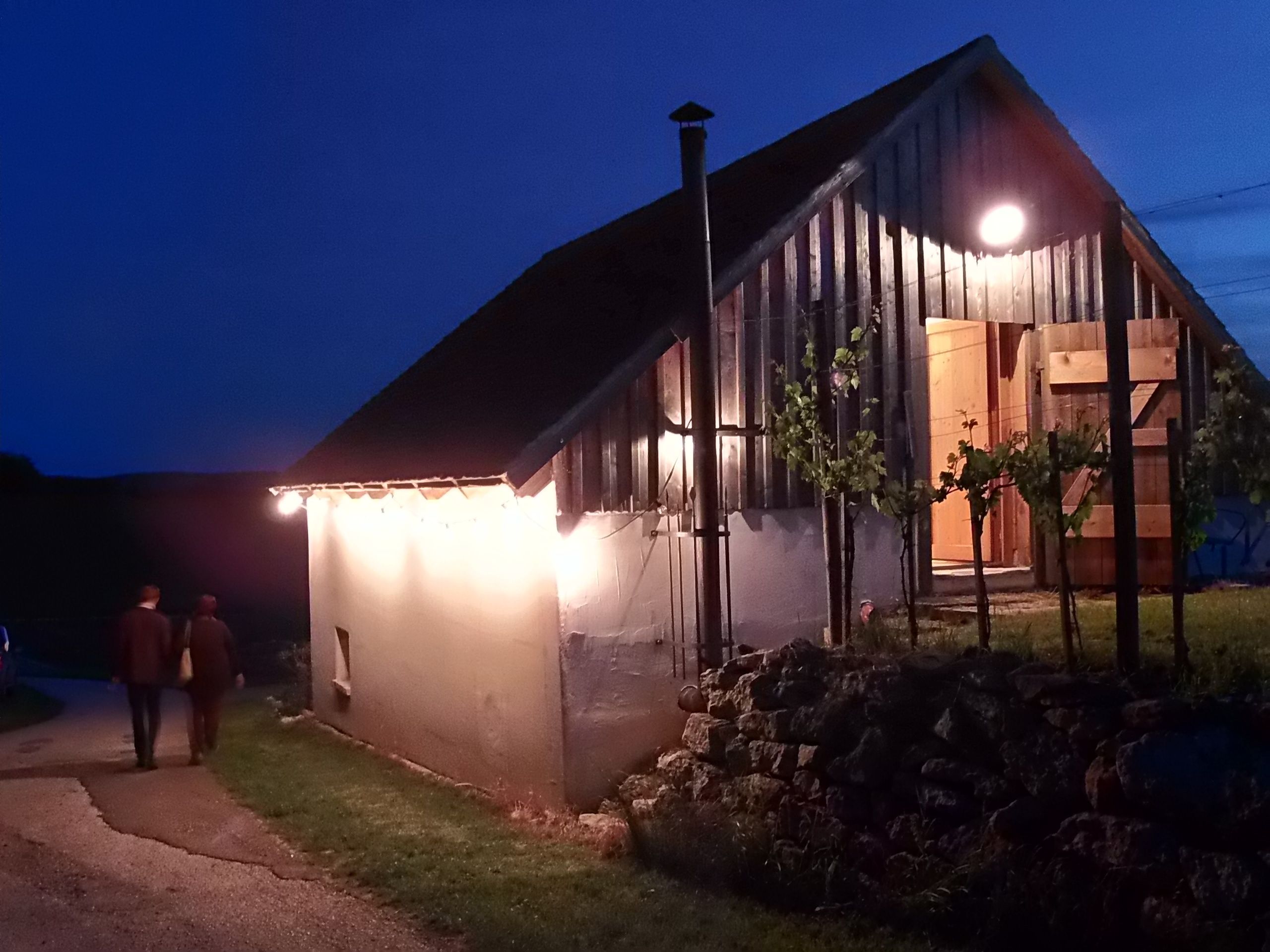 Beleuchtetes Weinkellergebäude bei Nacht mit zwei Personen auf einem Weg.