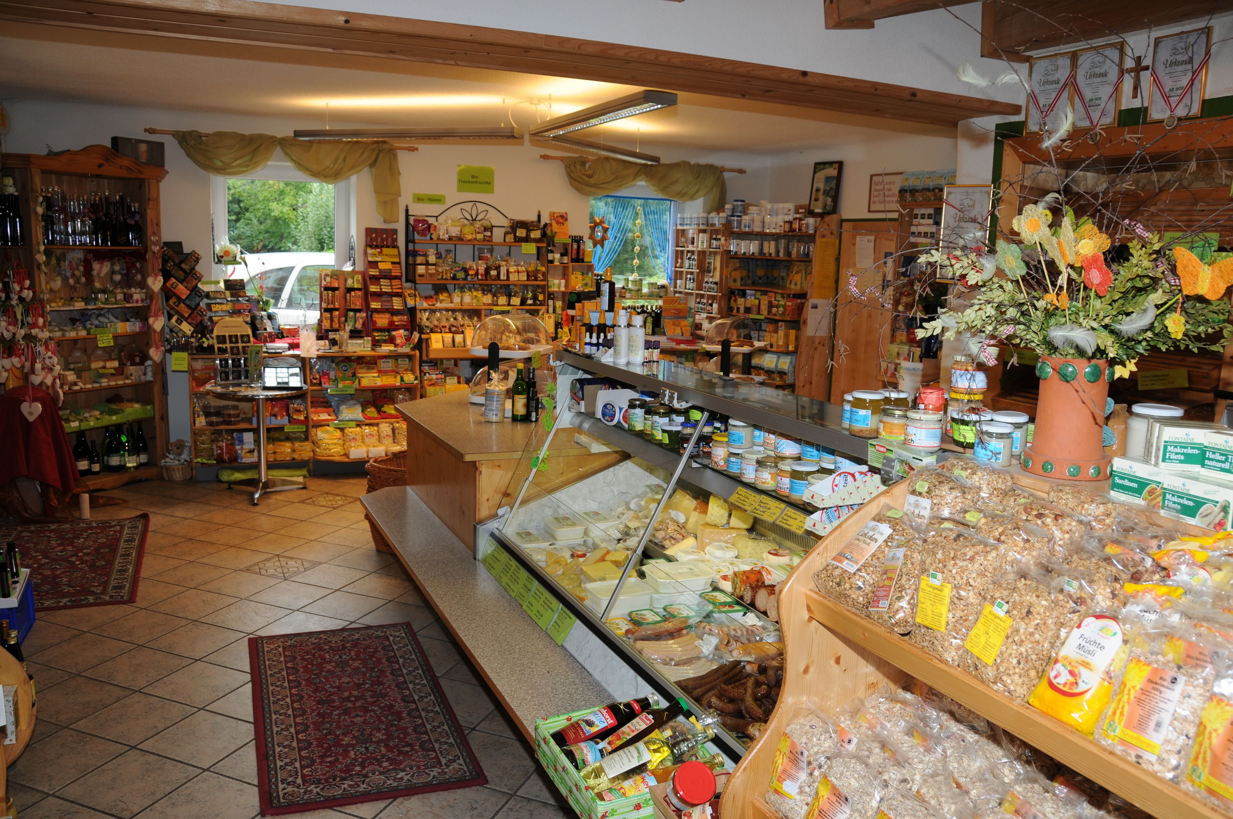 Innenansicht eines Bio-Hofladens mit Regalen voller Produkte und einer Theke mit Käse und Wurst.