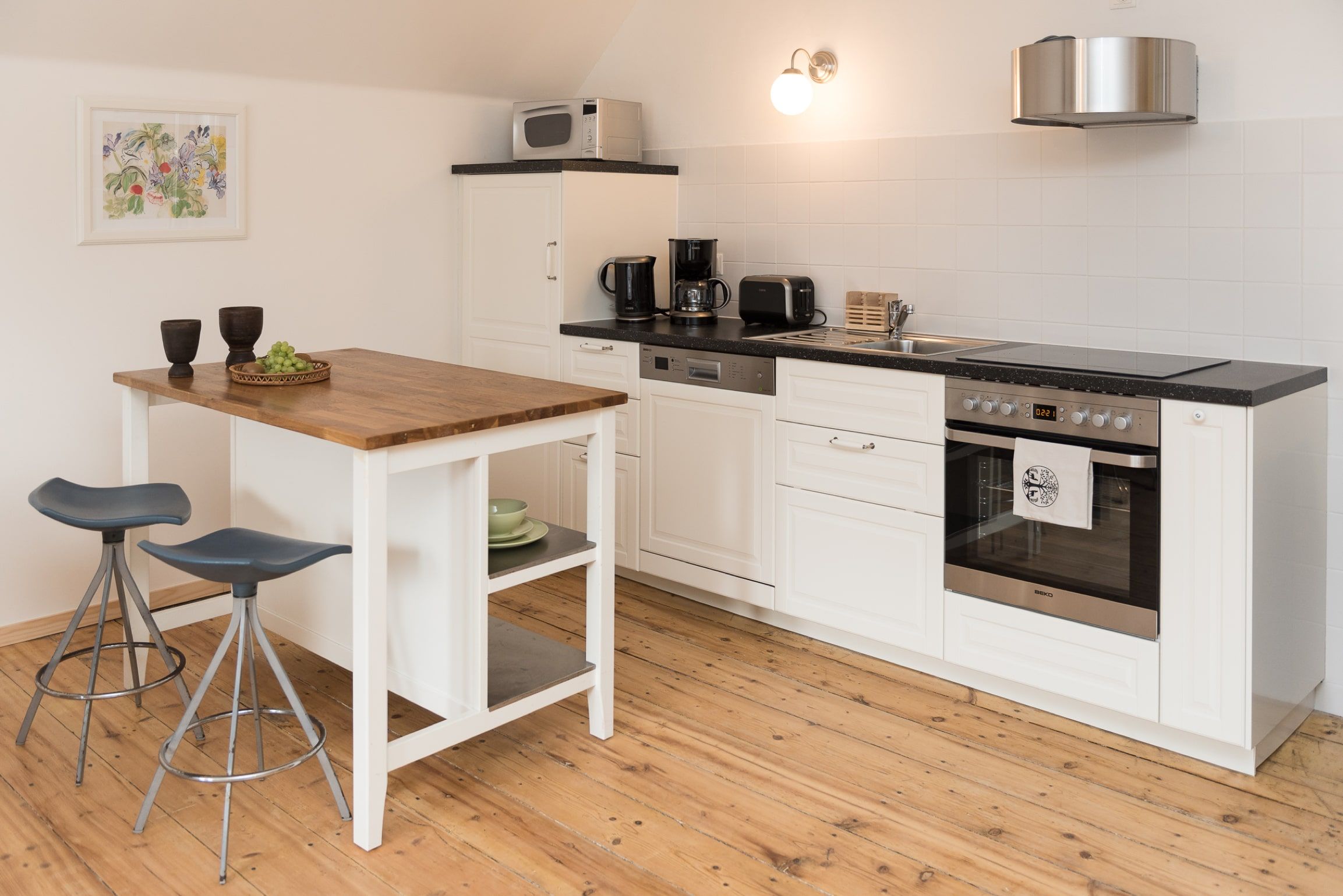 Moderne Küche mit weißer Einrichtung, Holzboden und kleinem Esstisch mit zwei Hockern.