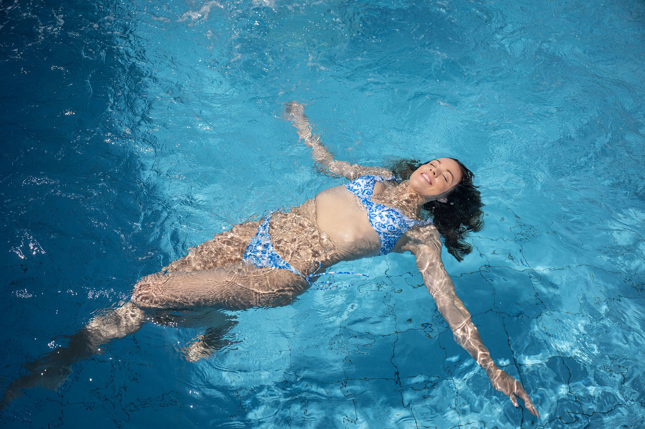 Frau in blauem Bikini treibt entspannt im Pool.