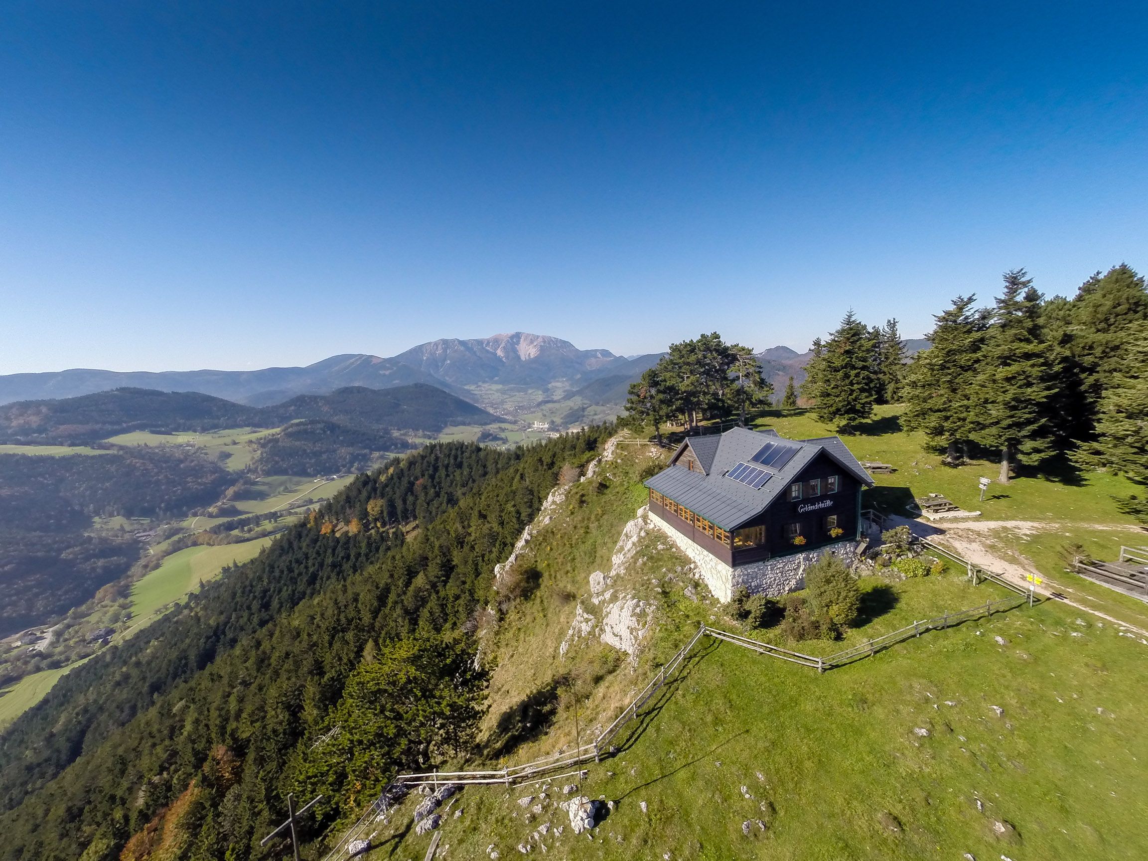 Hütte auf einem Hügel mit Berglandschaft im Hintergrund.