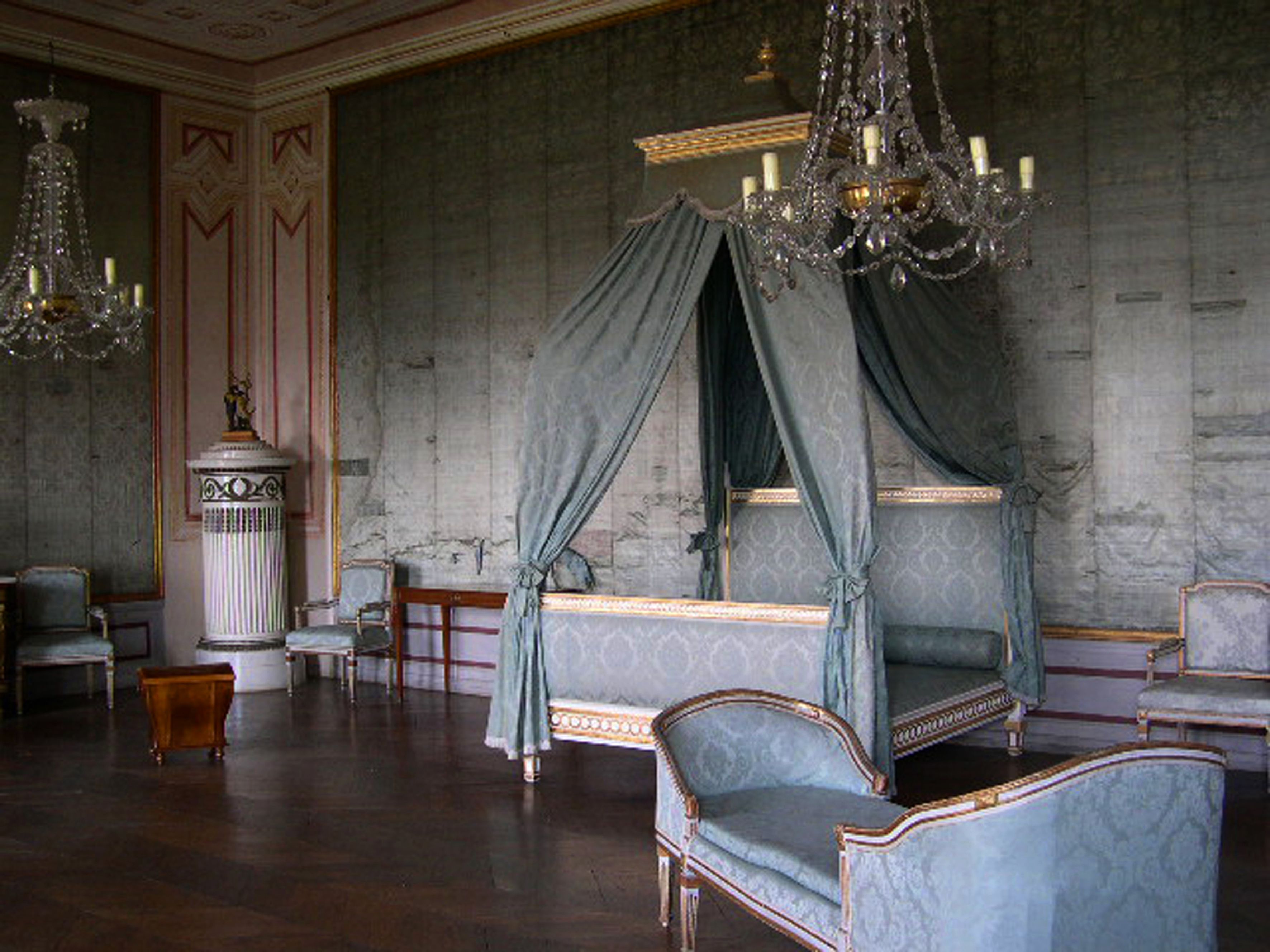 Ein elegantes Zimmer im Schloss Loosdorf mit einem Himmelbett, antiken Möbeln und Kronleuchtern.