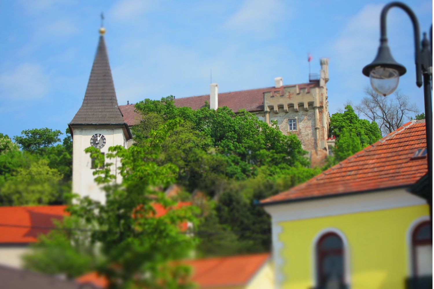 Kirchturm und Schloss hinter Bäumen, blauer Himmel.