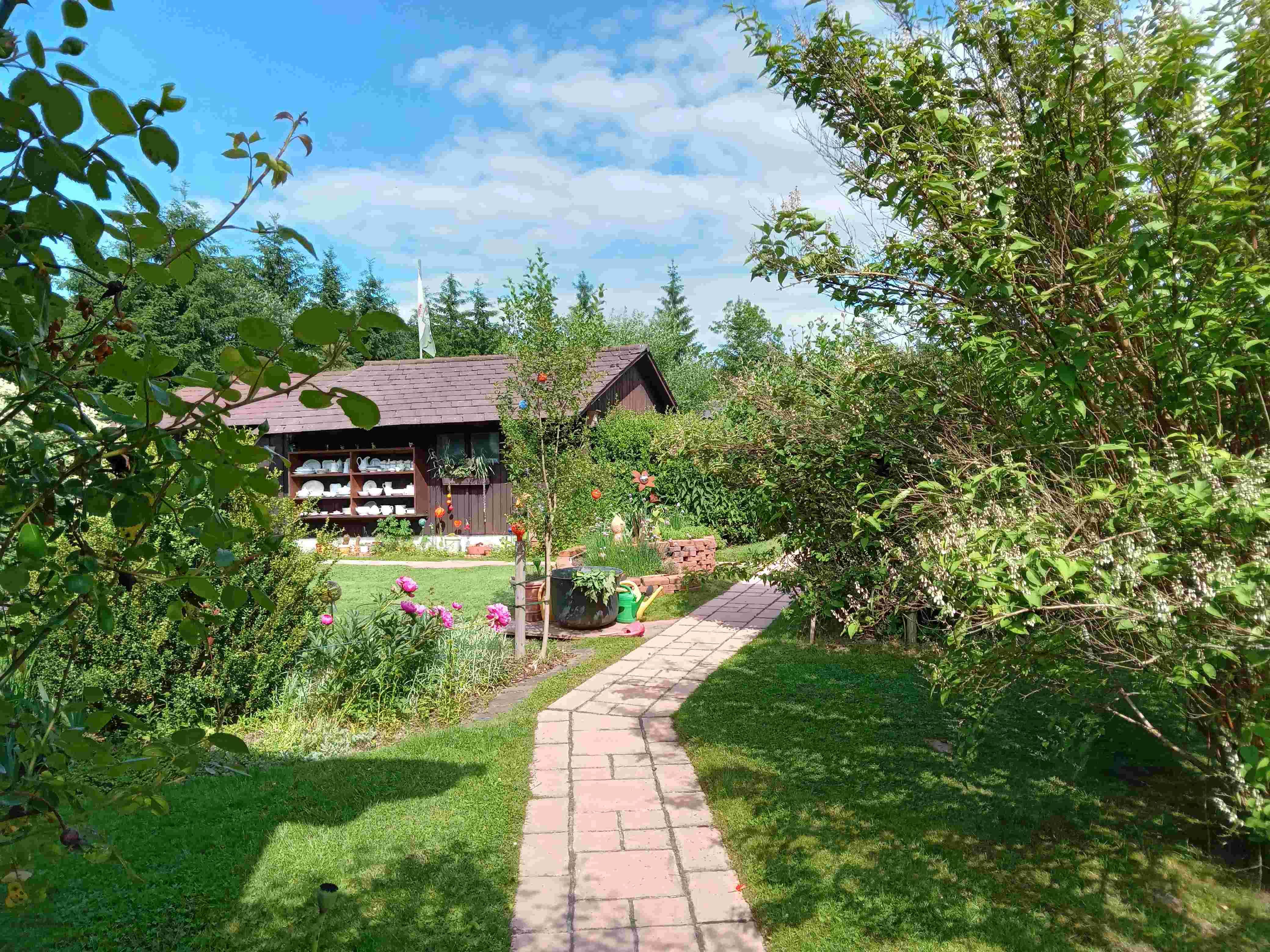 Garten mit Weg, Blumen und Holzhütte im Hintergrund.