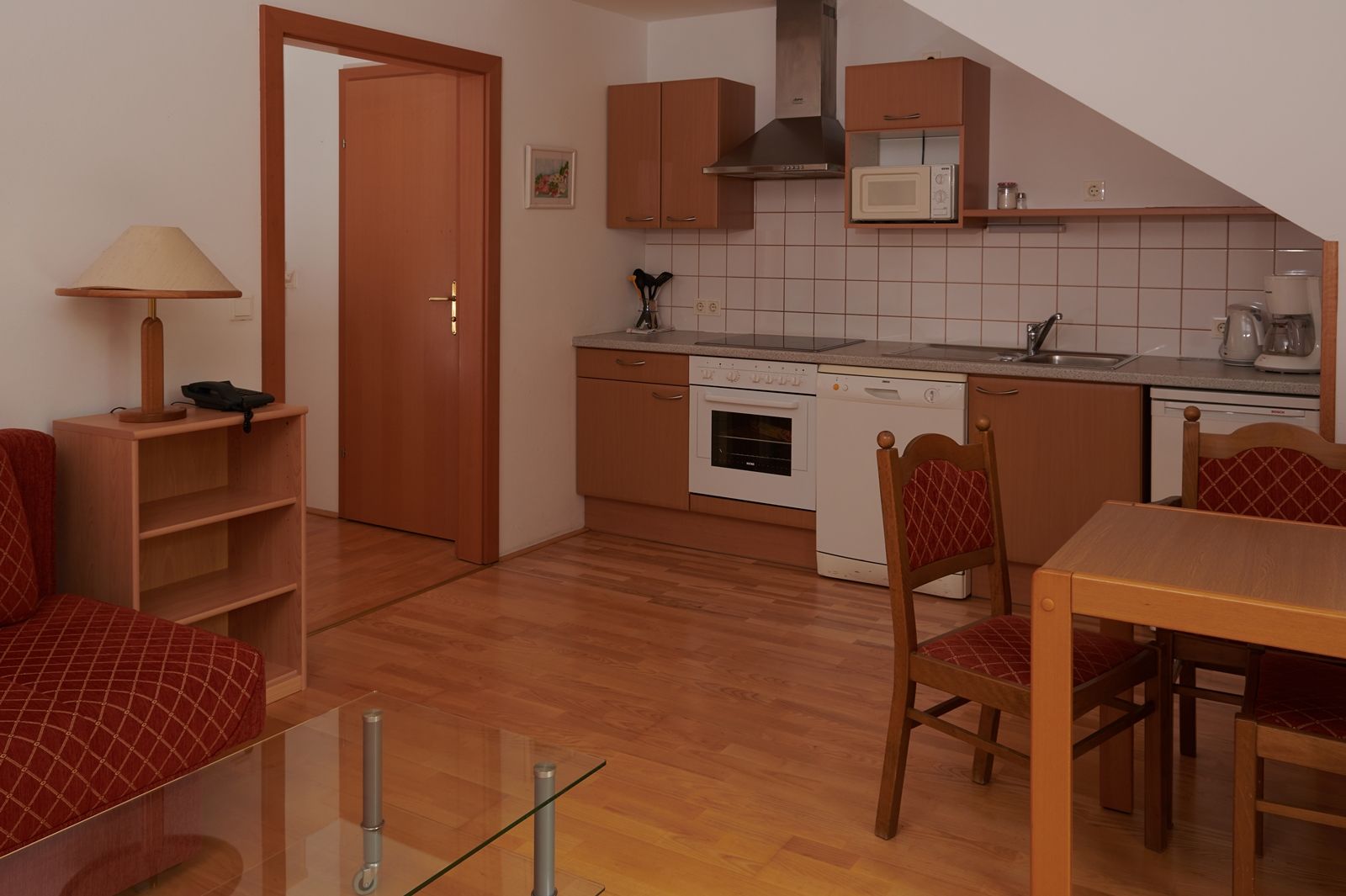 Kompakte Küche mit Holzschränken, Esstisch und Stühlen, Herd, Spüle und Mikrowelle.