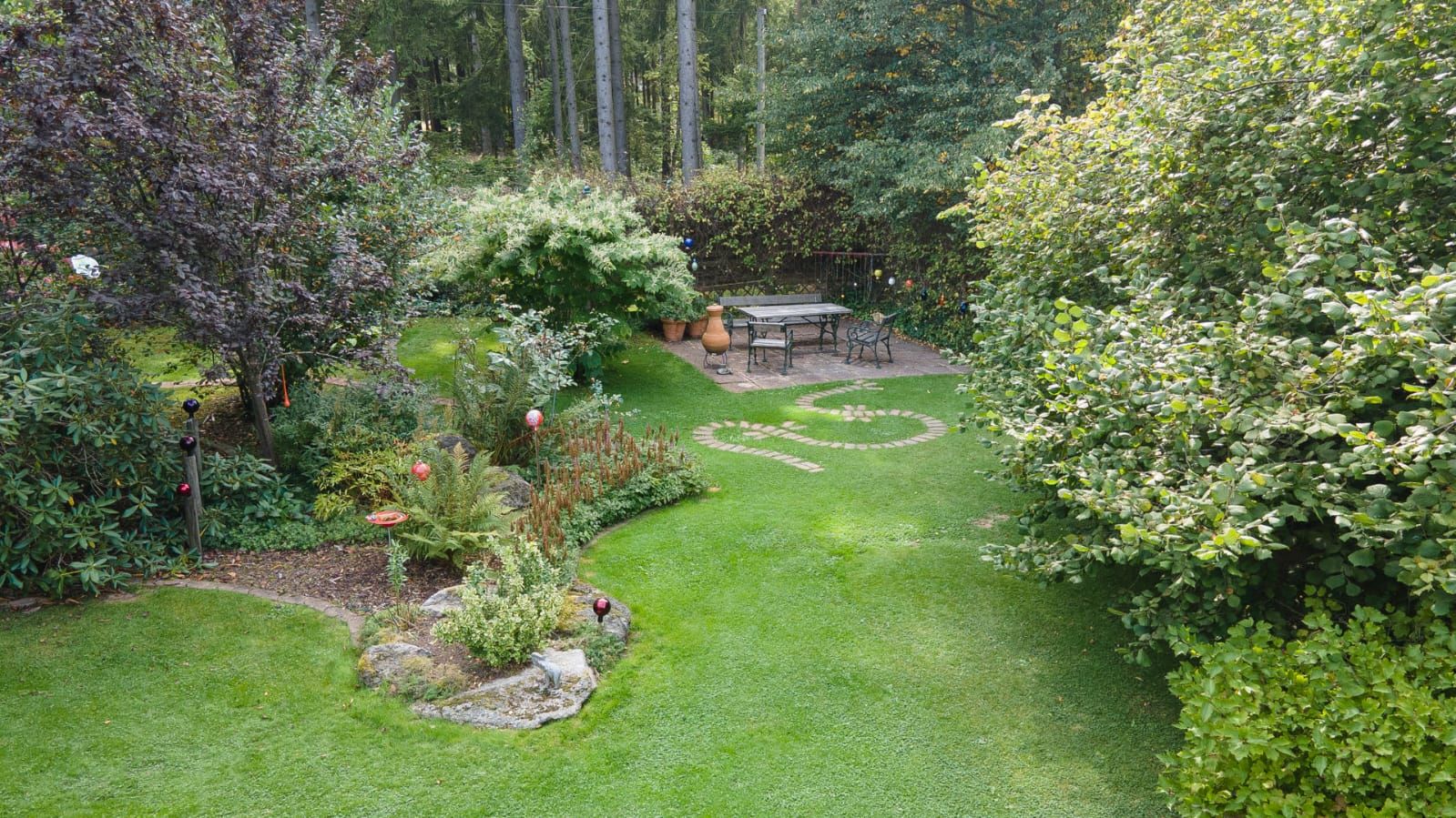 Ein gepflegter Garten mit Rasen, Bäumen und einem Sitzbereich auf einer Terrasse.