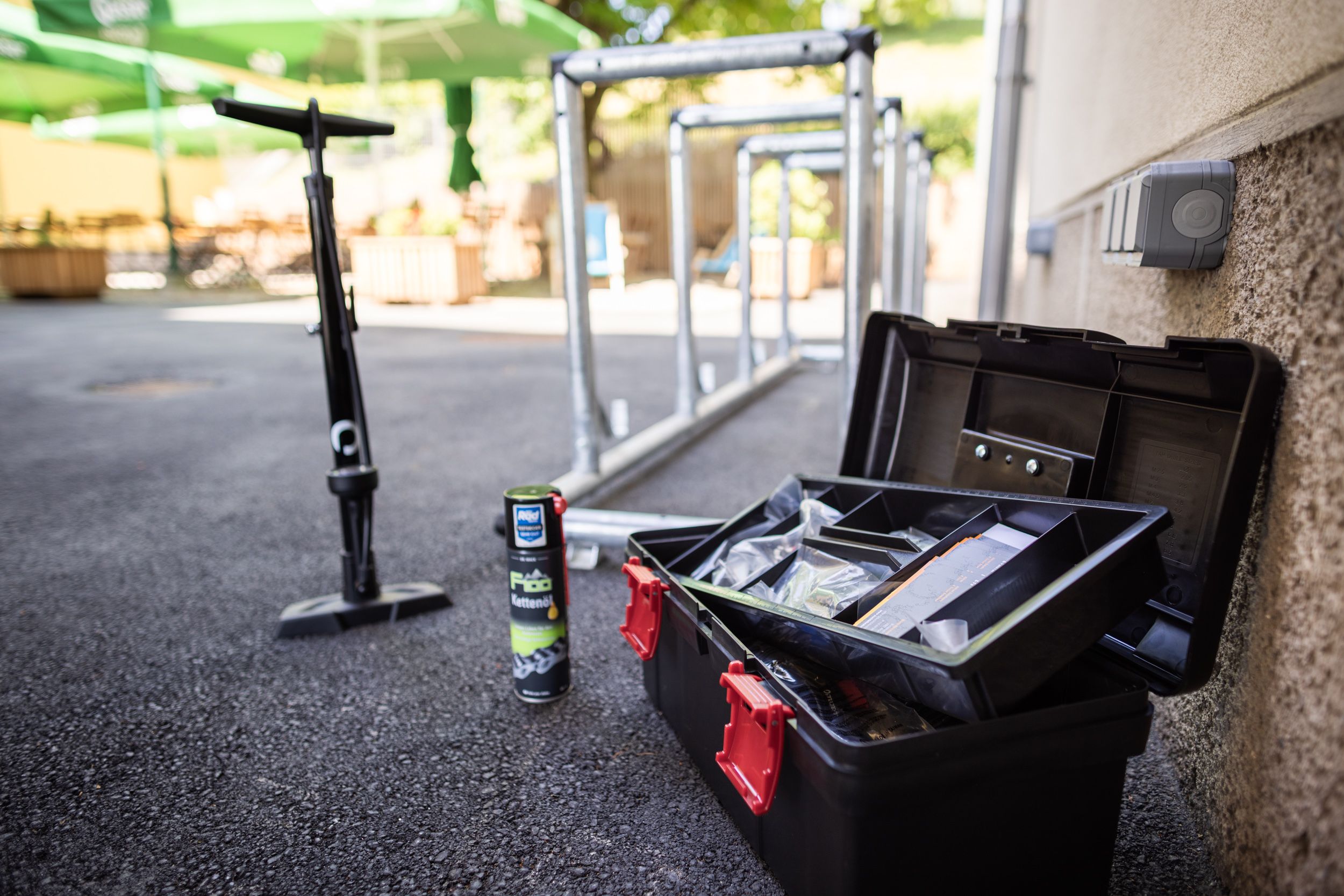 Fahrradwerkzeug, Kettenöl und Pumpe neben Fahrradständern im Freien.
