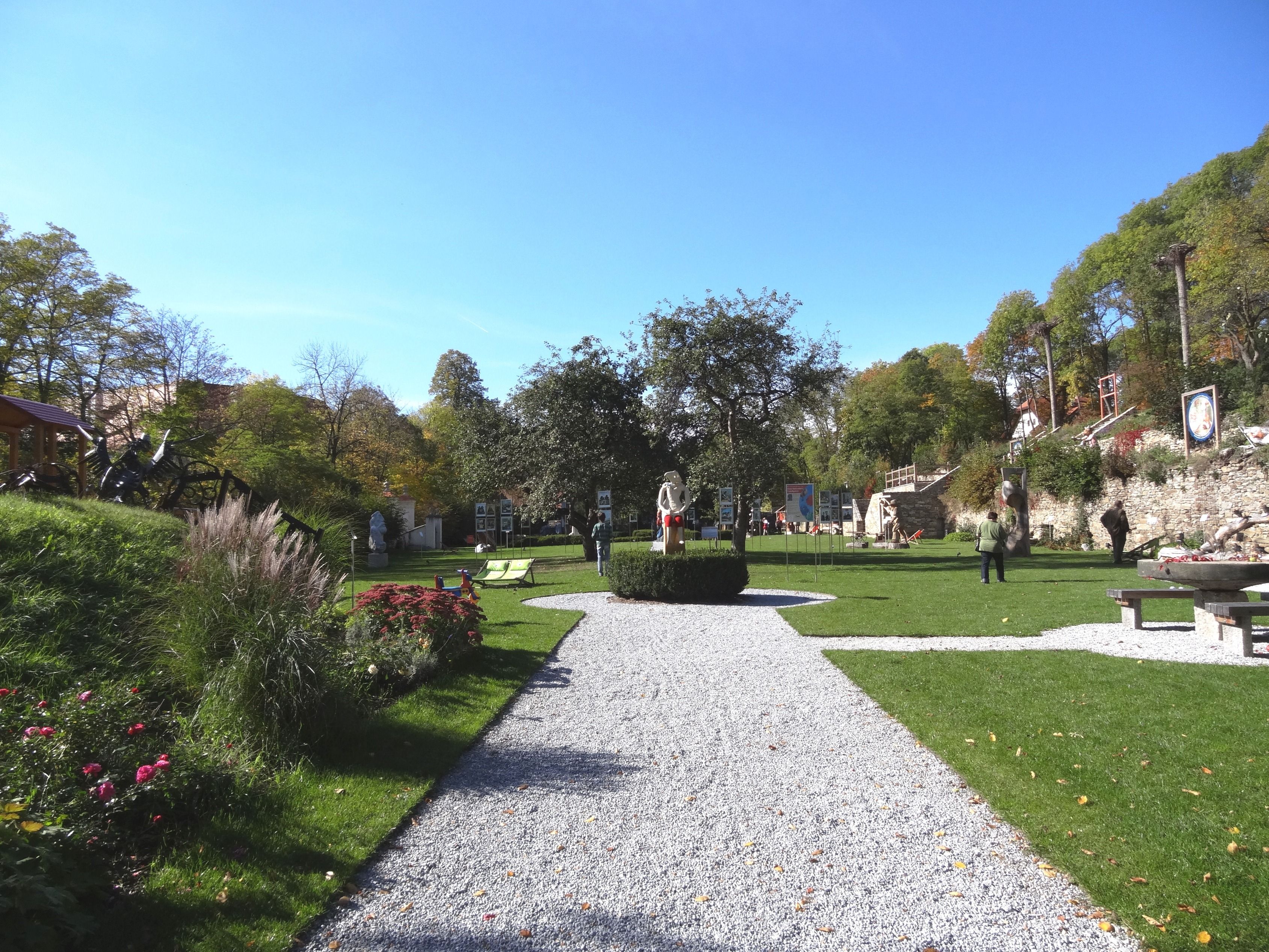 Ein gepflegter Garten mit Skulpturen und Spaziergängern bei sonnigem Wetter.