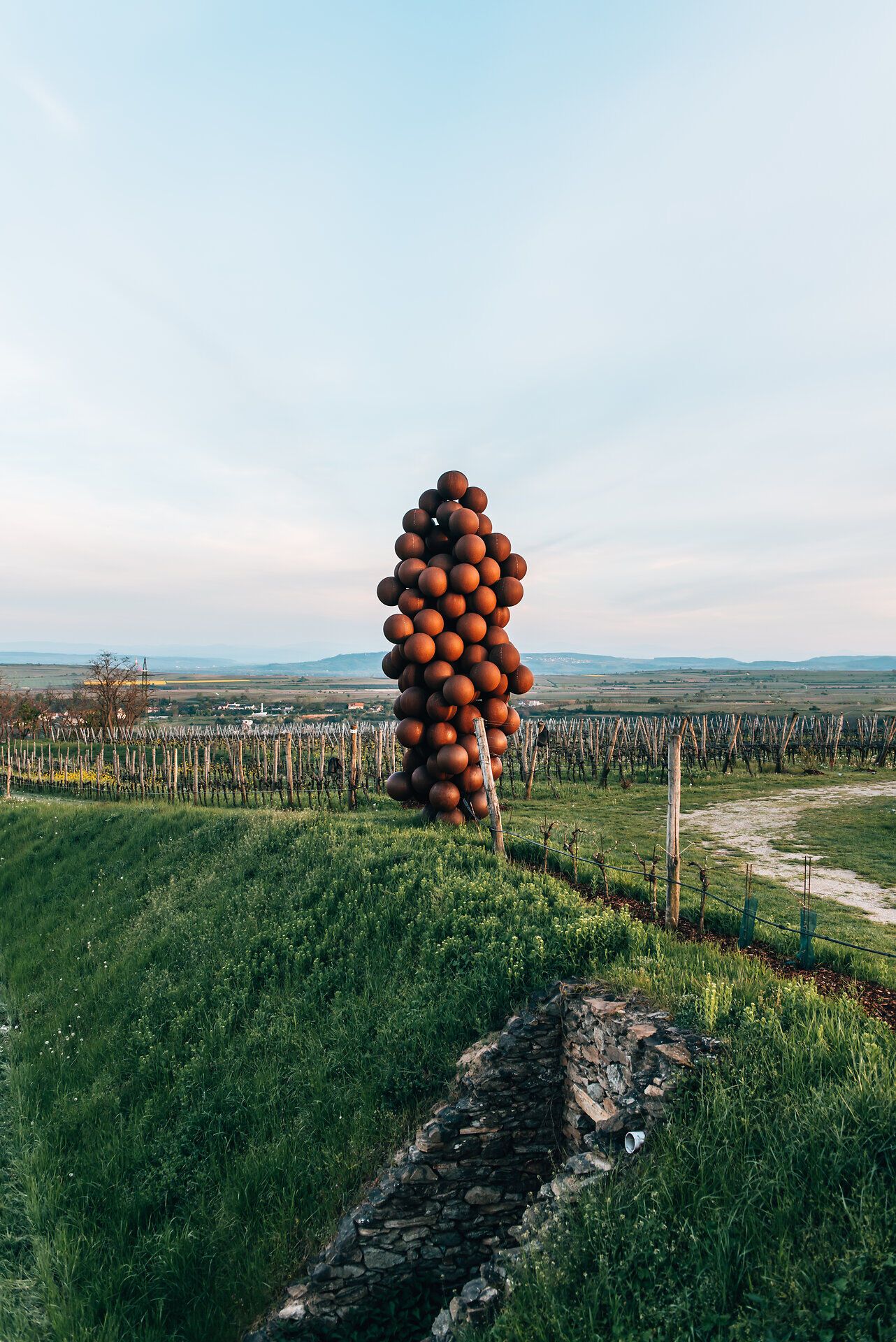 Eine beeindruckende Skulptur aus zahlreichen Weintrauben erhebt sich majestätisch über die sanften Hügel der Weinregion. Die harmonische Verbindung von Kunst und Natur lädt dazu ein, innezuhalten und die Schönheit der Umgebung zu genießen. Hier, wo die Weinreben in der Abendsonne leuchten, wird der Sommer in den Bergen zum unvergesslichen Erlebnis.