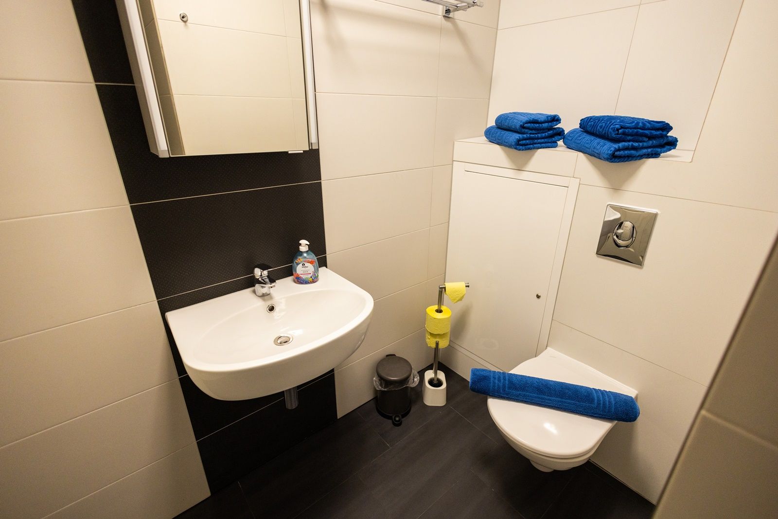 Kleines Badezimmer mit Waschbecken, Toilette, blauen Handtüchern und gelbem Toilettenpapier.